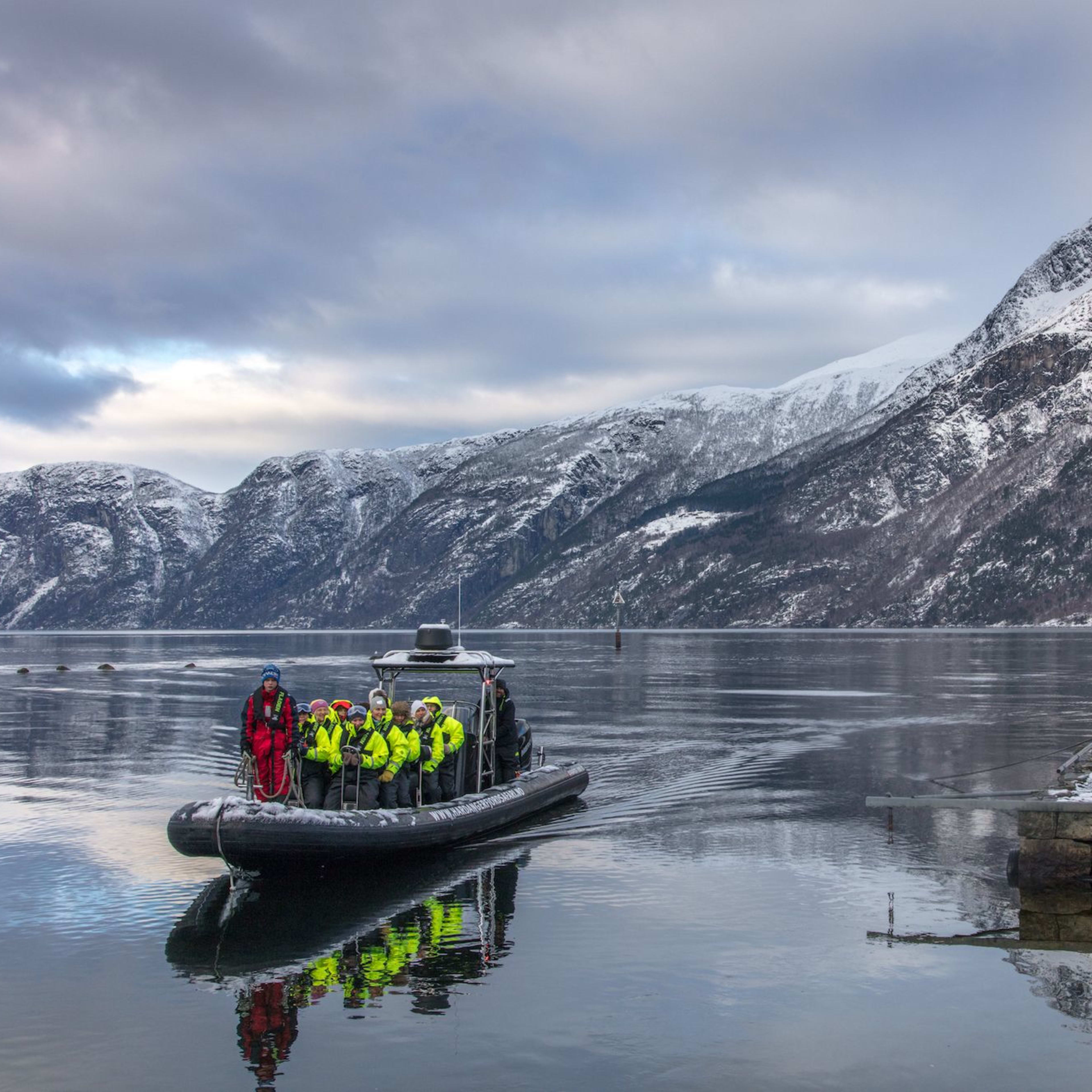 Passengers in a RIB boat on the Hardangerfjord from Eidfjord near a snowy dock and mountains.