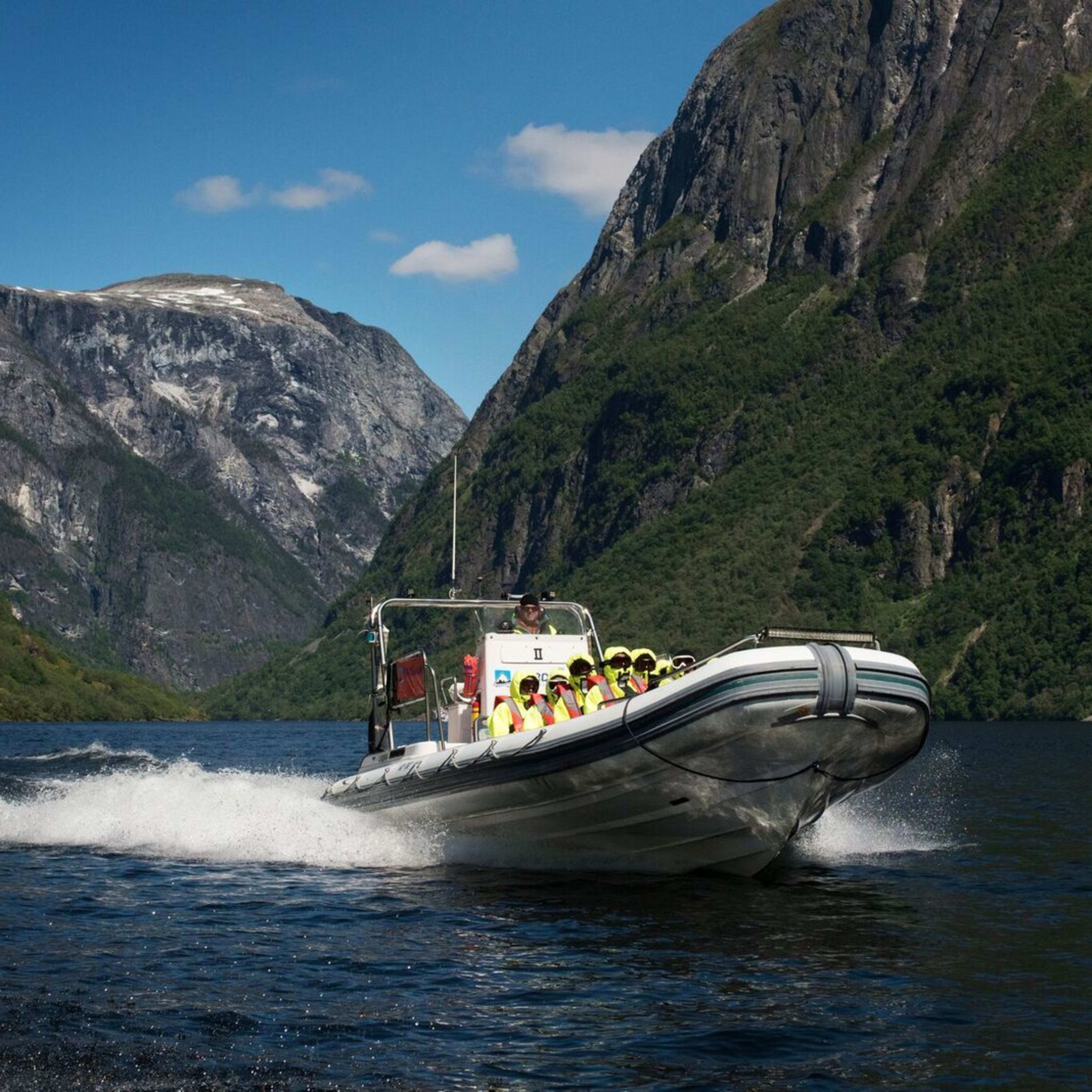 Båt med passasjerer i gult suser over mørk fjord.