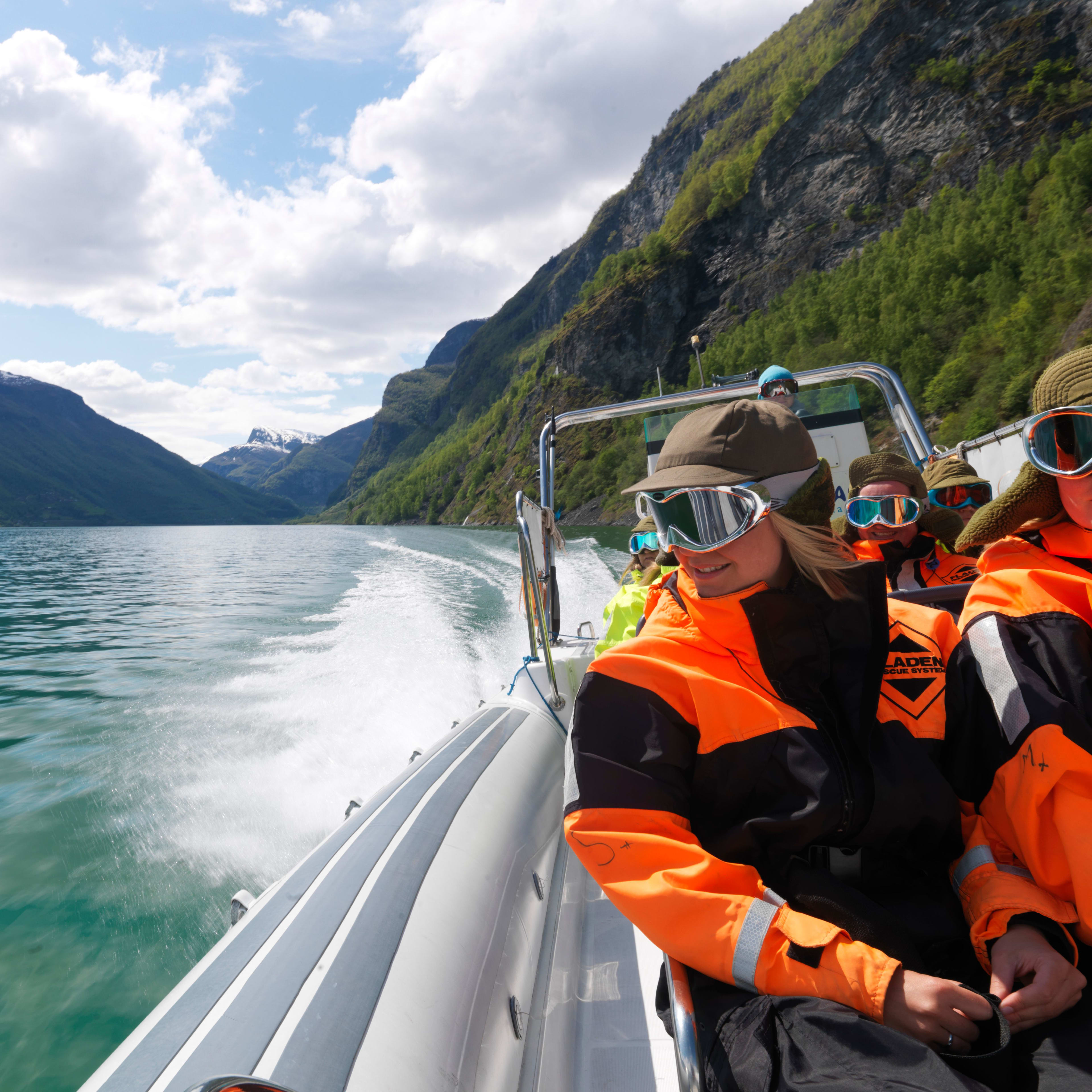 Passasjerer i overlevelsesdrakter kjører en høyhastighets RIB-båt på Nærøyfjorden