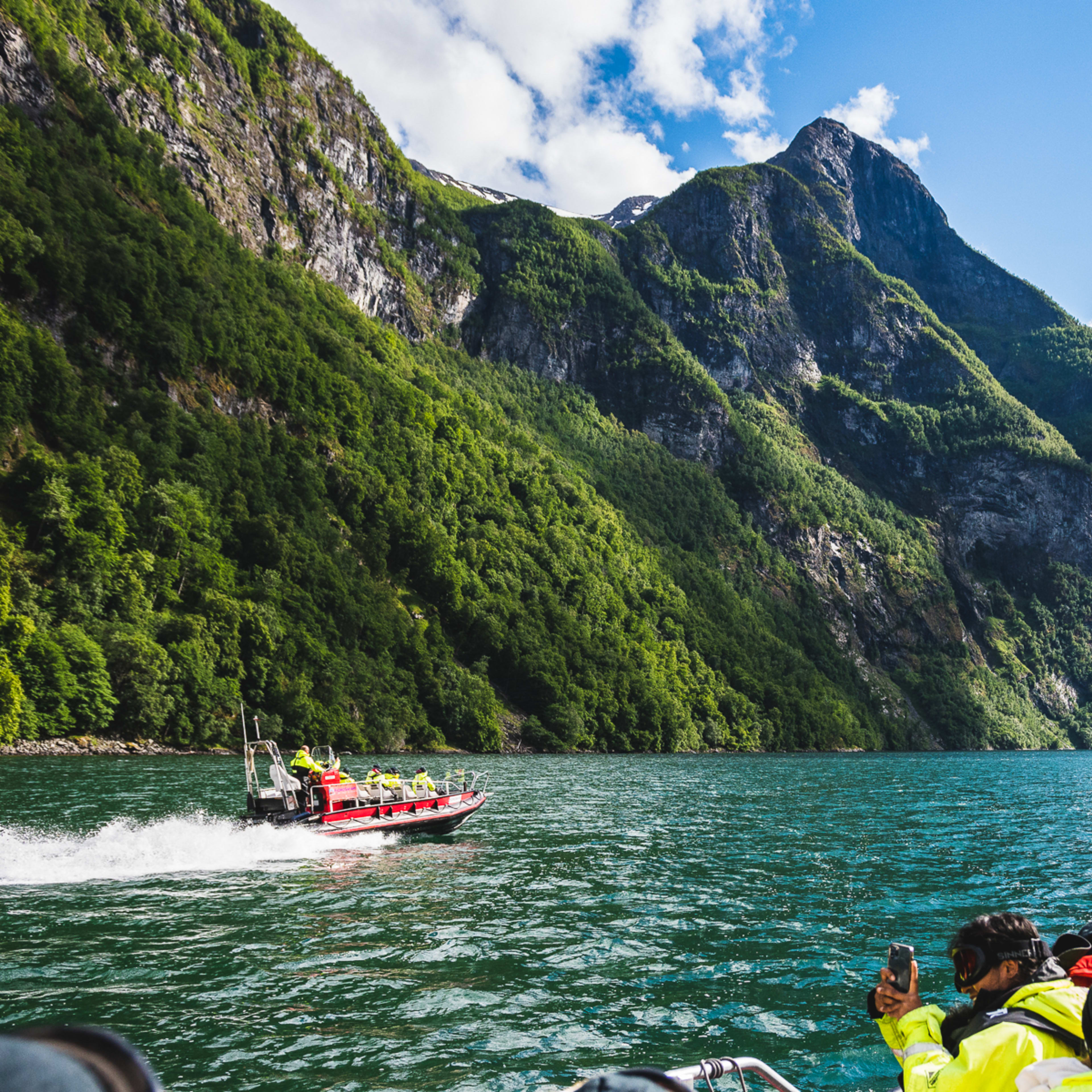 Fjord safari boats sailing on Nærøyfjord toward Sagofossen waterfall near Flåm on a sunny summer day