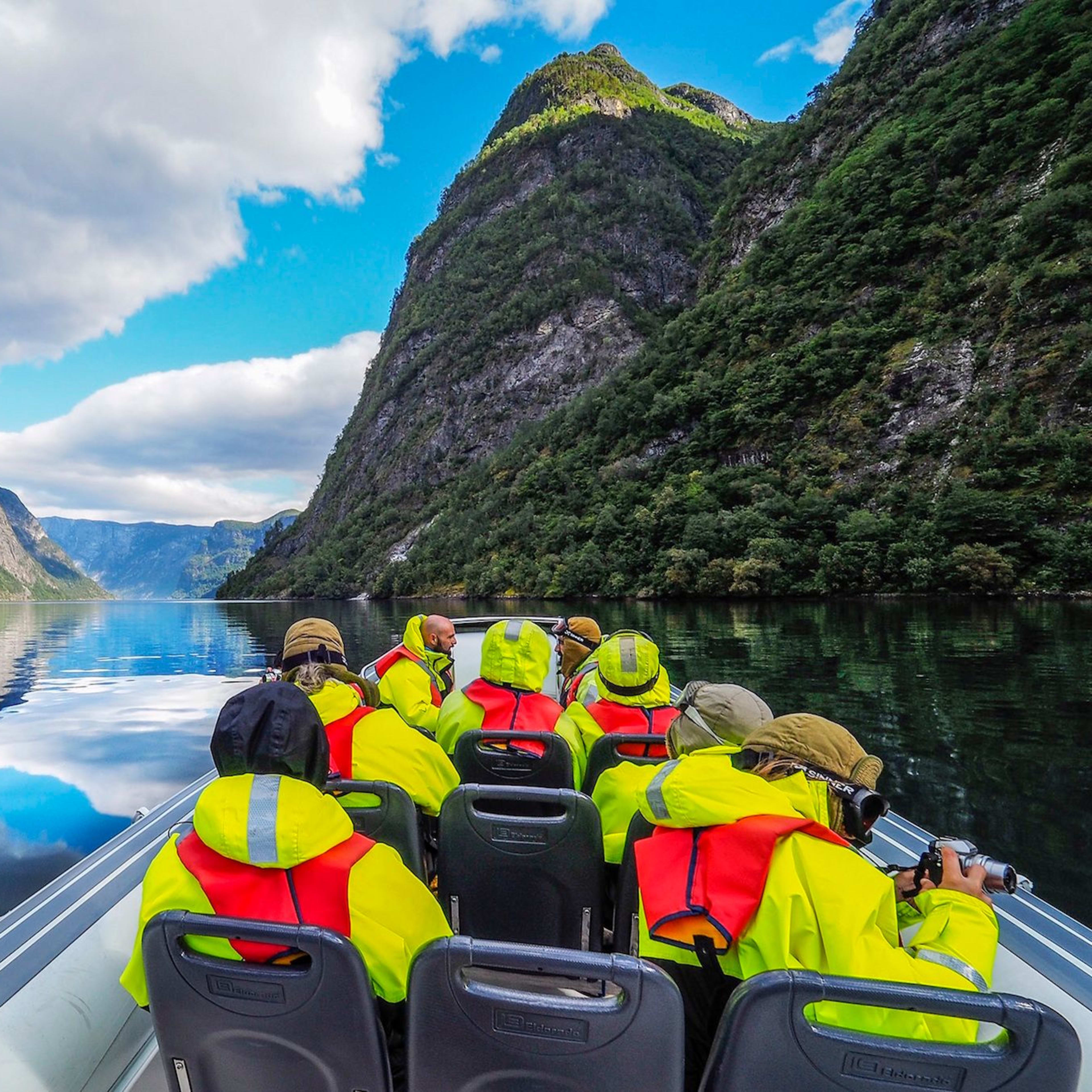Menschen auf einer Rib-Boot-Safari im wunderschönen Nærøyfjord mit spiegelnden Klippen und bewölktem Himmel.