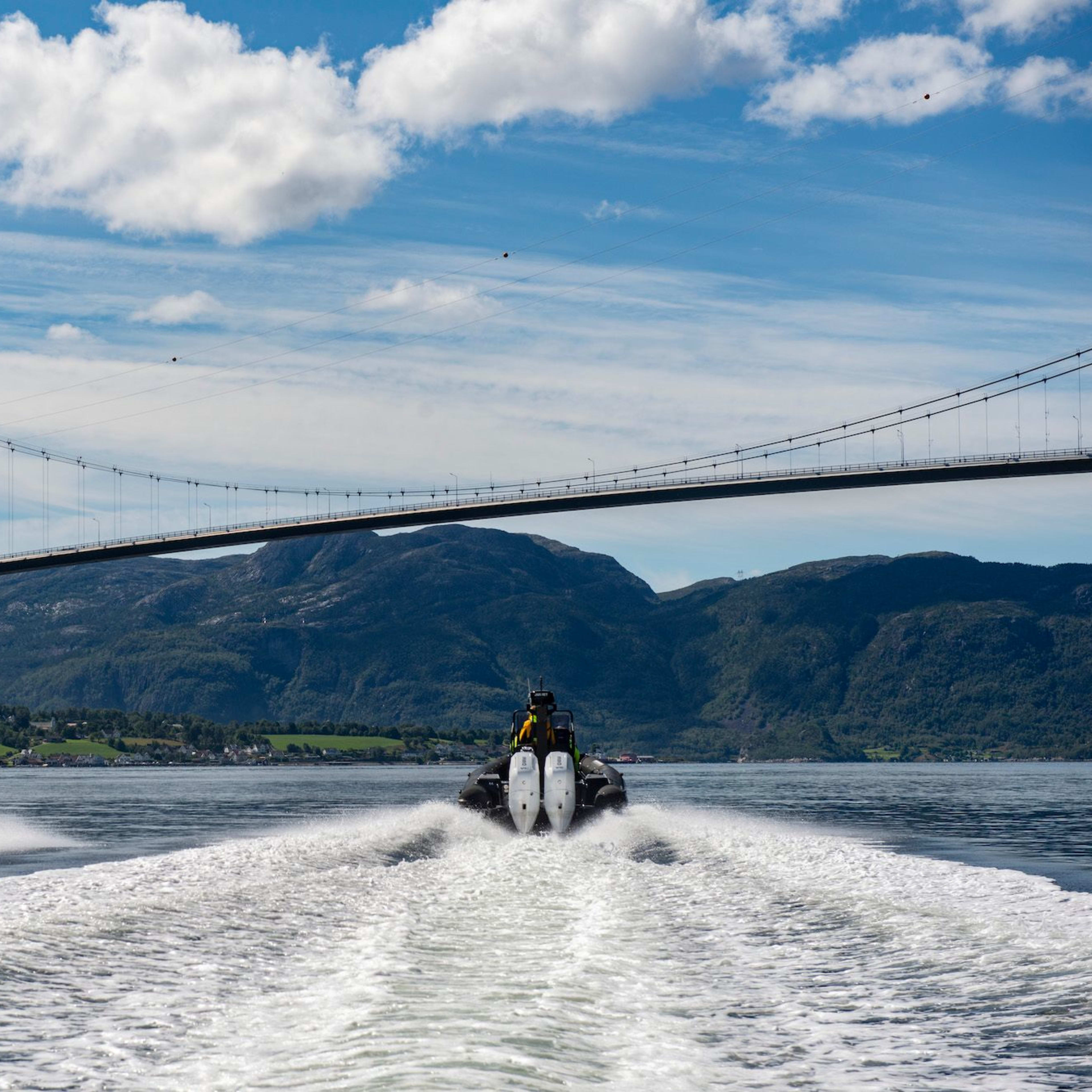 RIB-Boote auf dem Lysefjord mit einer Hängebrücke und grünen Bergen im Hintergrund.