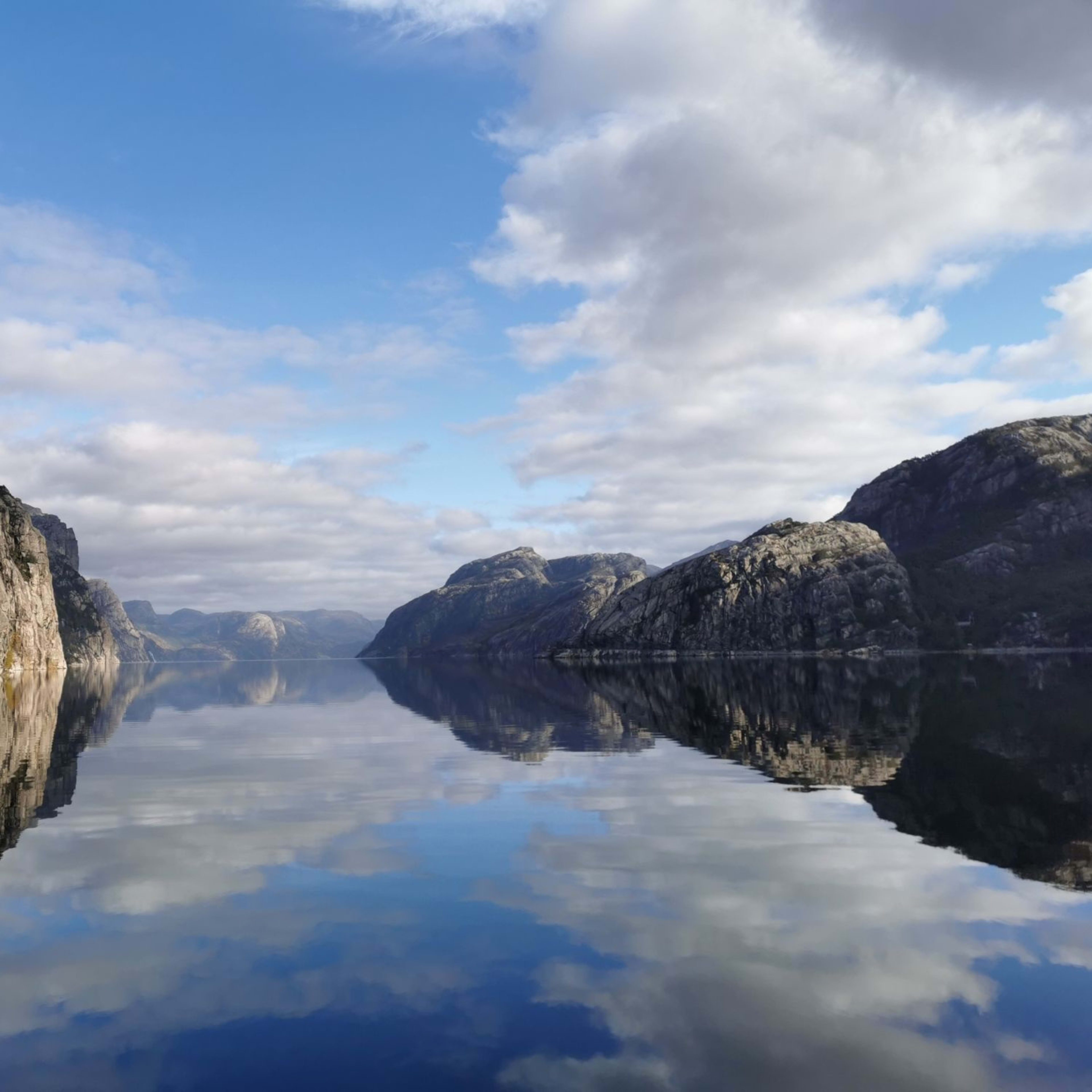 Hohe Klippen und Wolken spiegeln sich im glasklaren Wasser des Lysefjords.