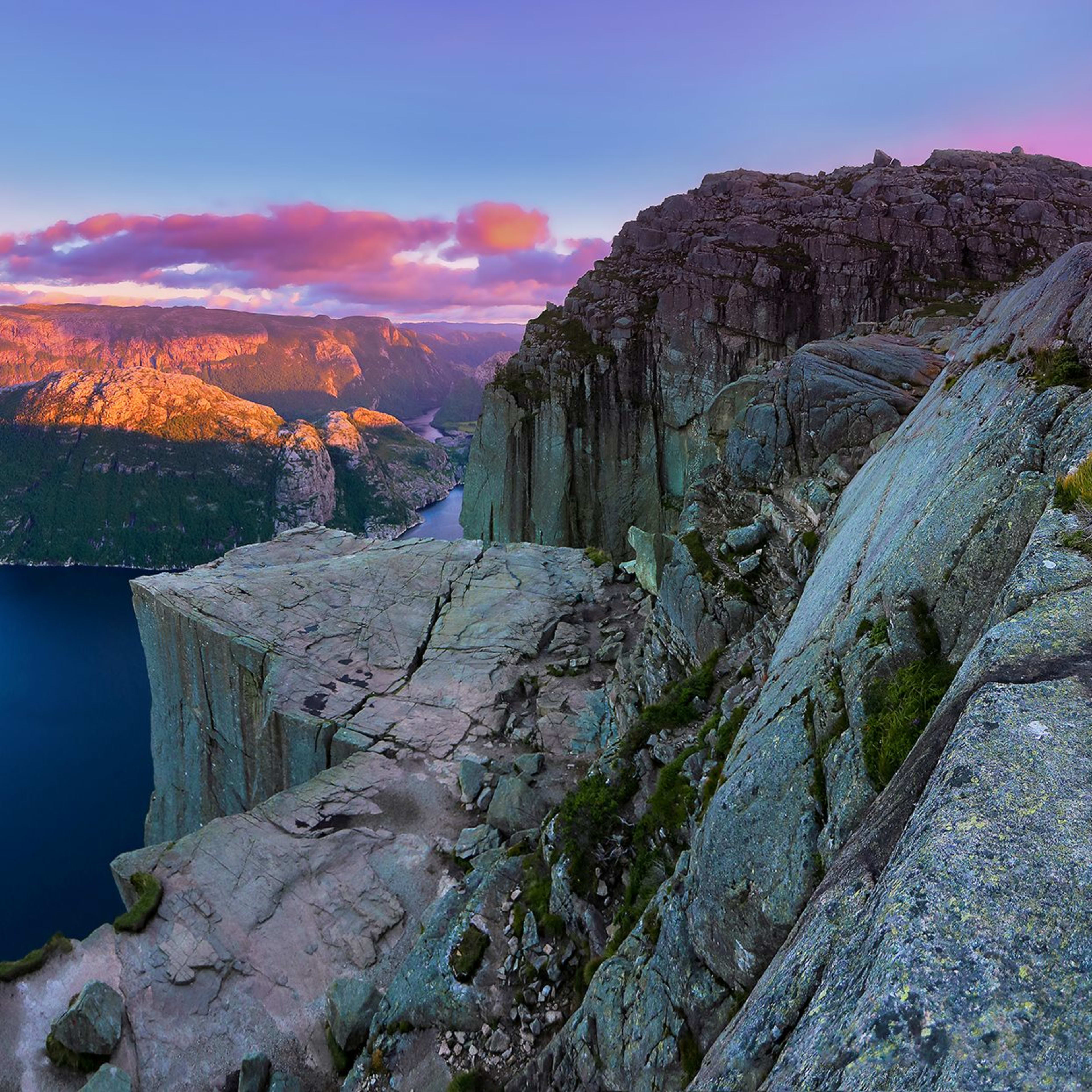 Preikestolen-Blick auf den Lysefjord bei Sonnenuntergang mit warmem Licht auf schroffen Gipfeln unter einem farbenfrohen Himmel.
