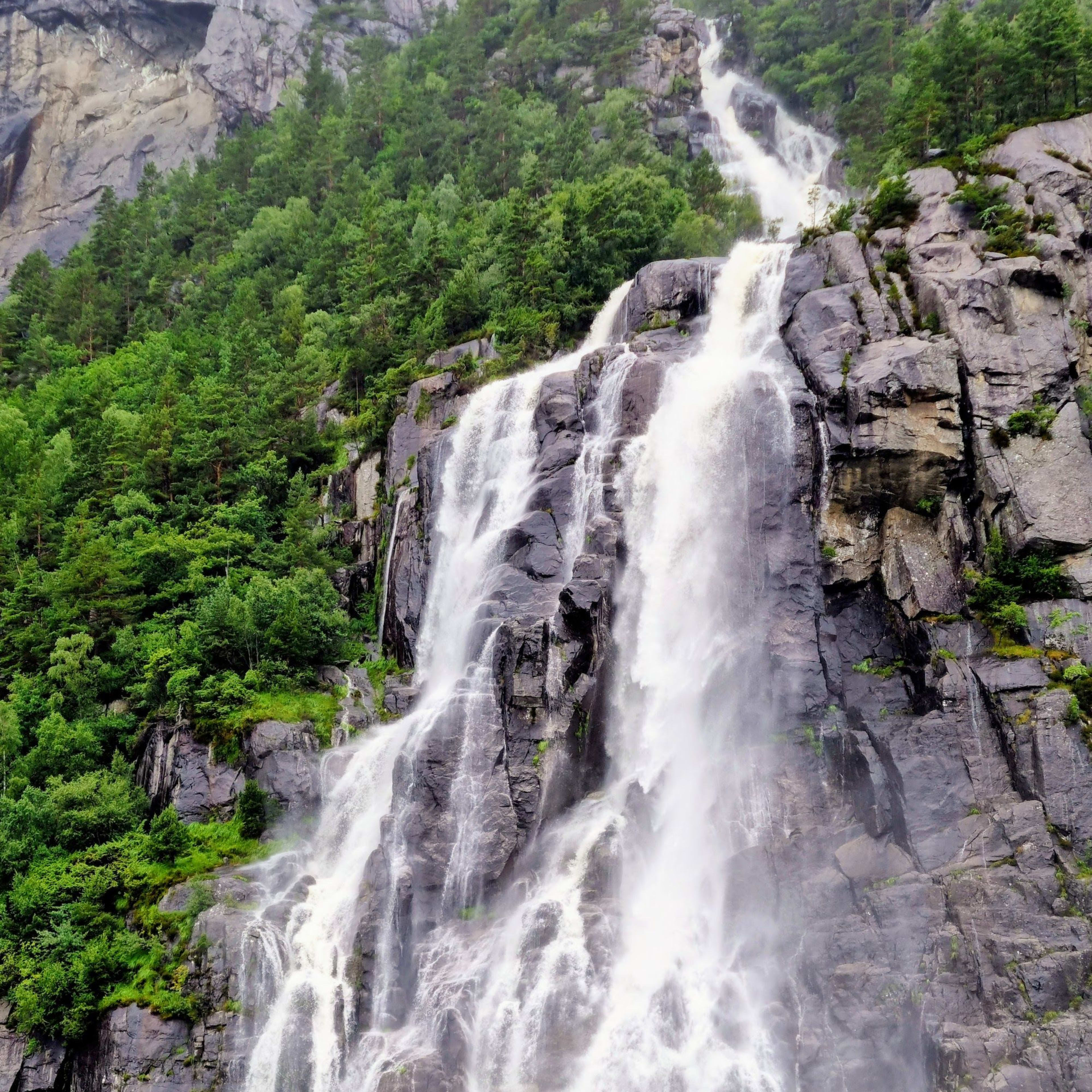 Ein gewaltiger Wasserfall ergießt sich in den Lysefjord. Nebel steigt auf und Passagiere in einem Boot beobachten die großartige Naturschönheit.