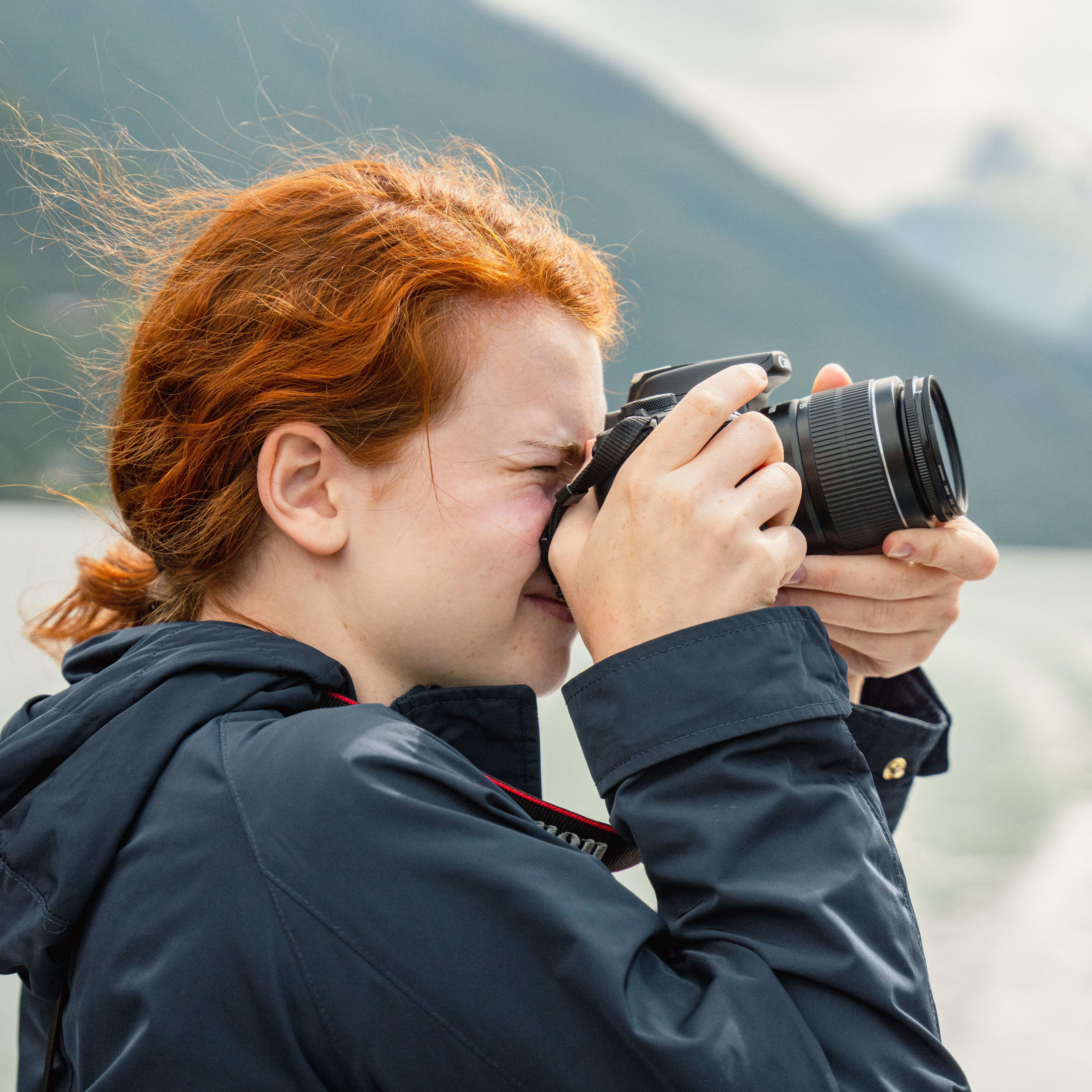 Person with red hair photographs misty Sognefjord landscape from boat.