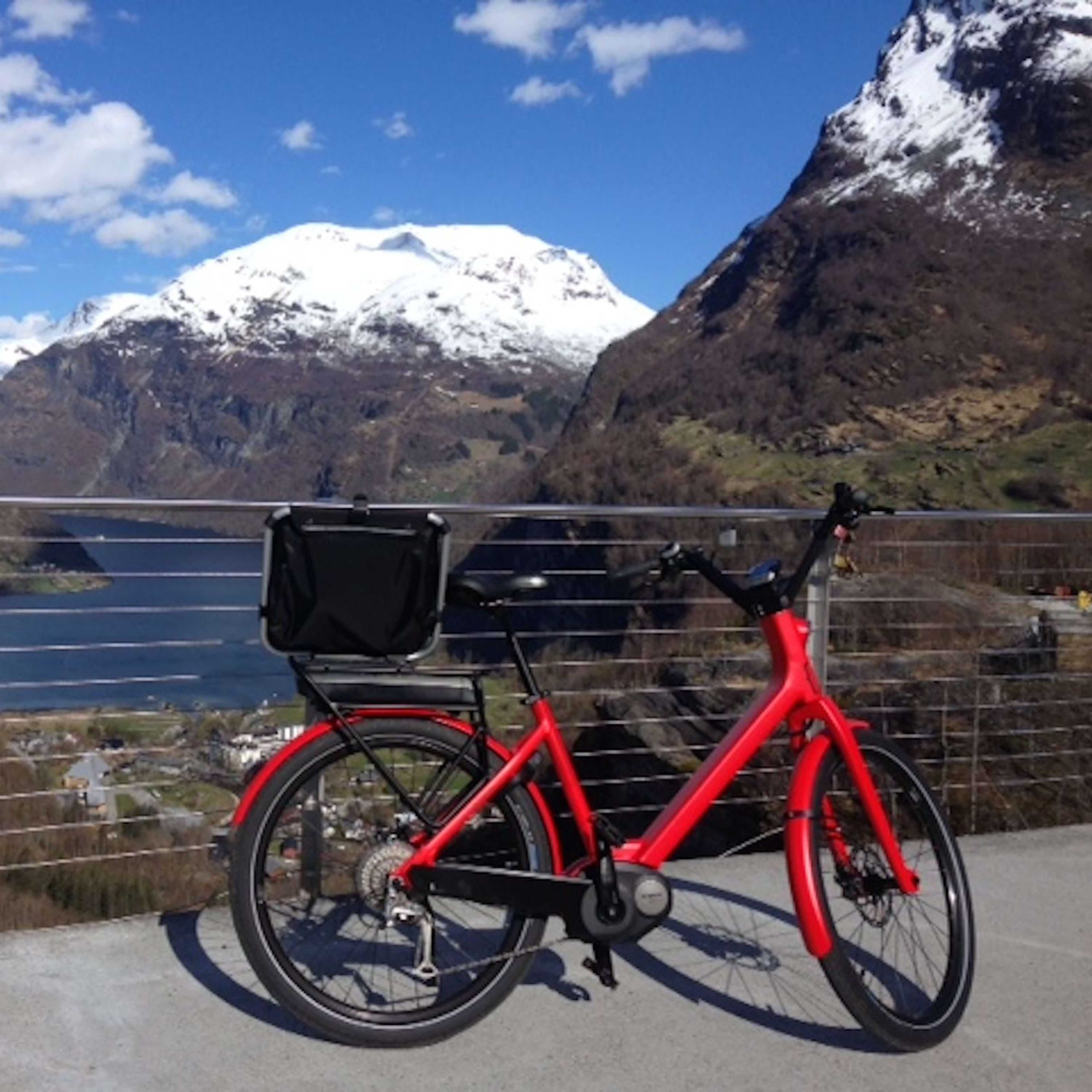 Rotes E-Bike mit Gepäckbox auf Terrasse mit Fjordblick.