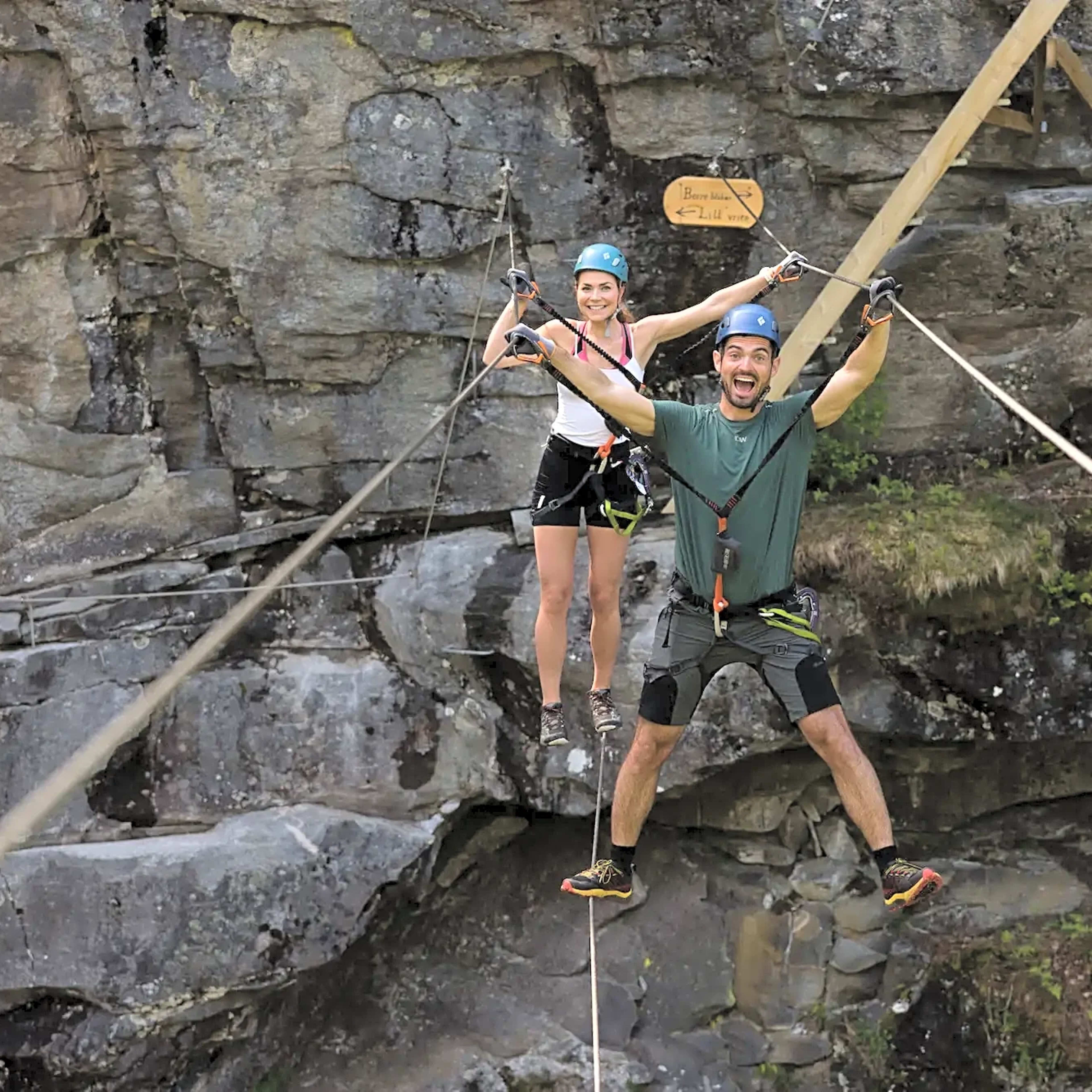 Mann og kvinne krysser eventyr-bro på fjellvegg på Geiranger park