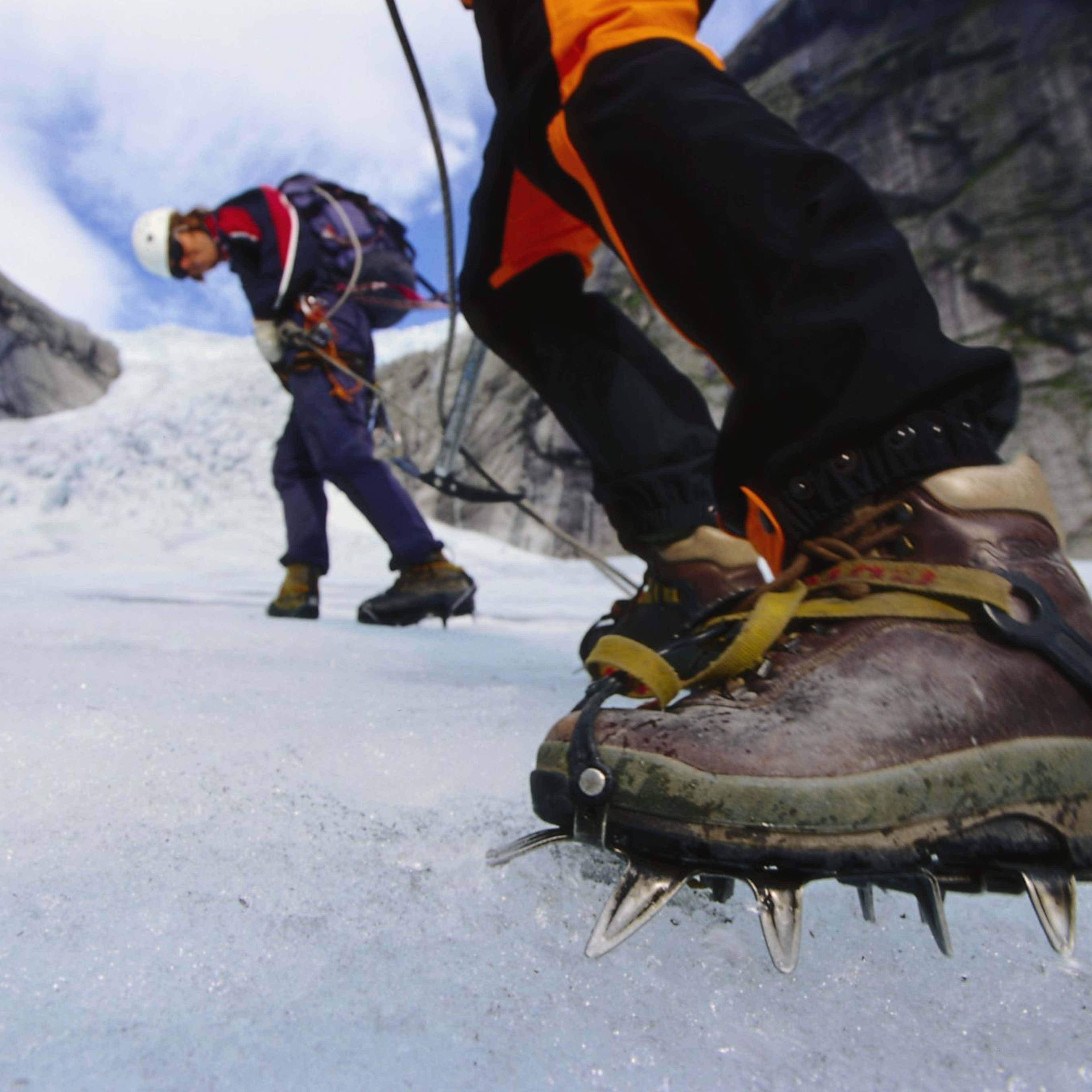Two climbers making their way up a glacier, with ice axes and crampons, rugged glacier landscape in background.