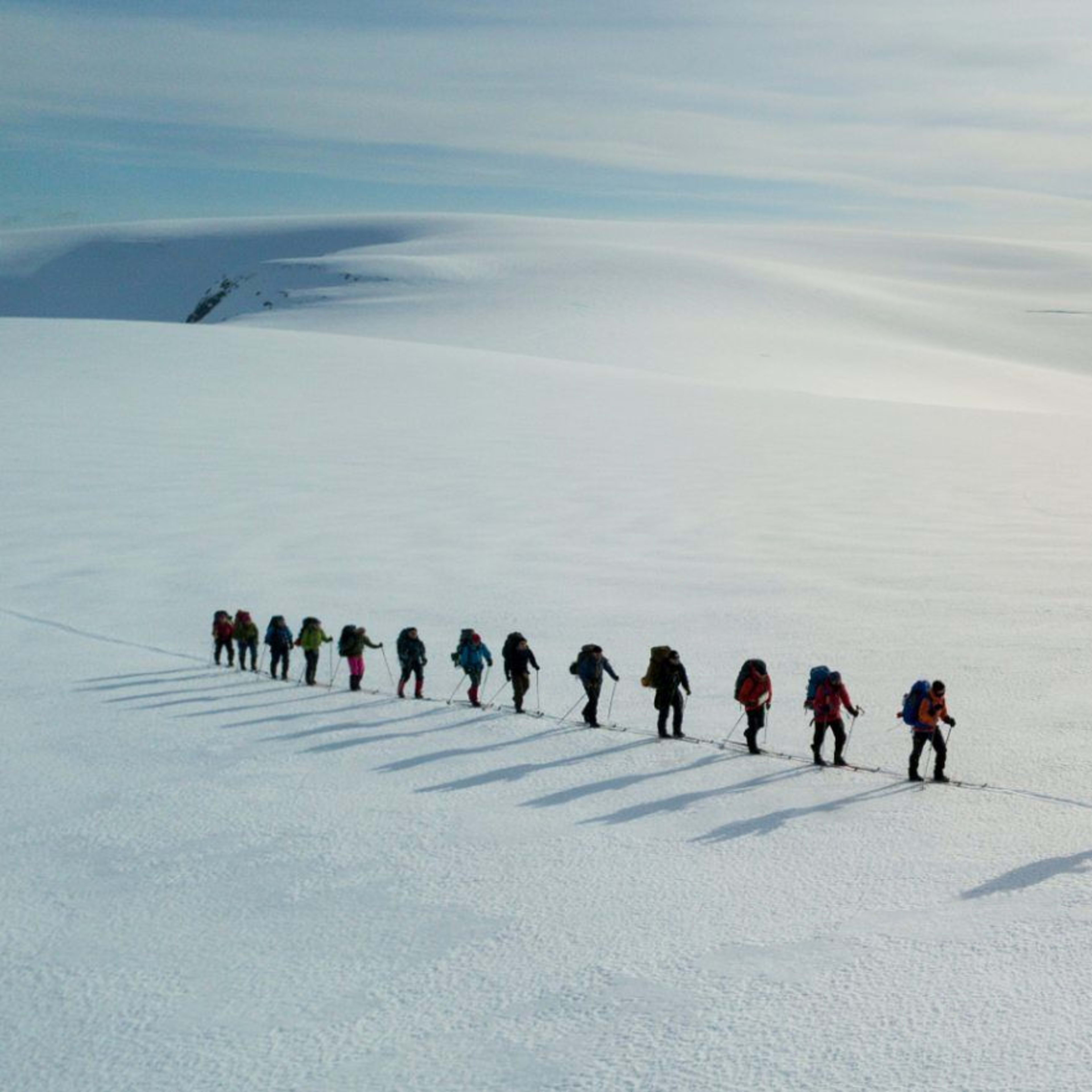 Gruppe von Skifahrern mit großen Rucksäcken, die durch eine schneebedeckte Landschaft fahren, mit Bergen im Hintergrund.