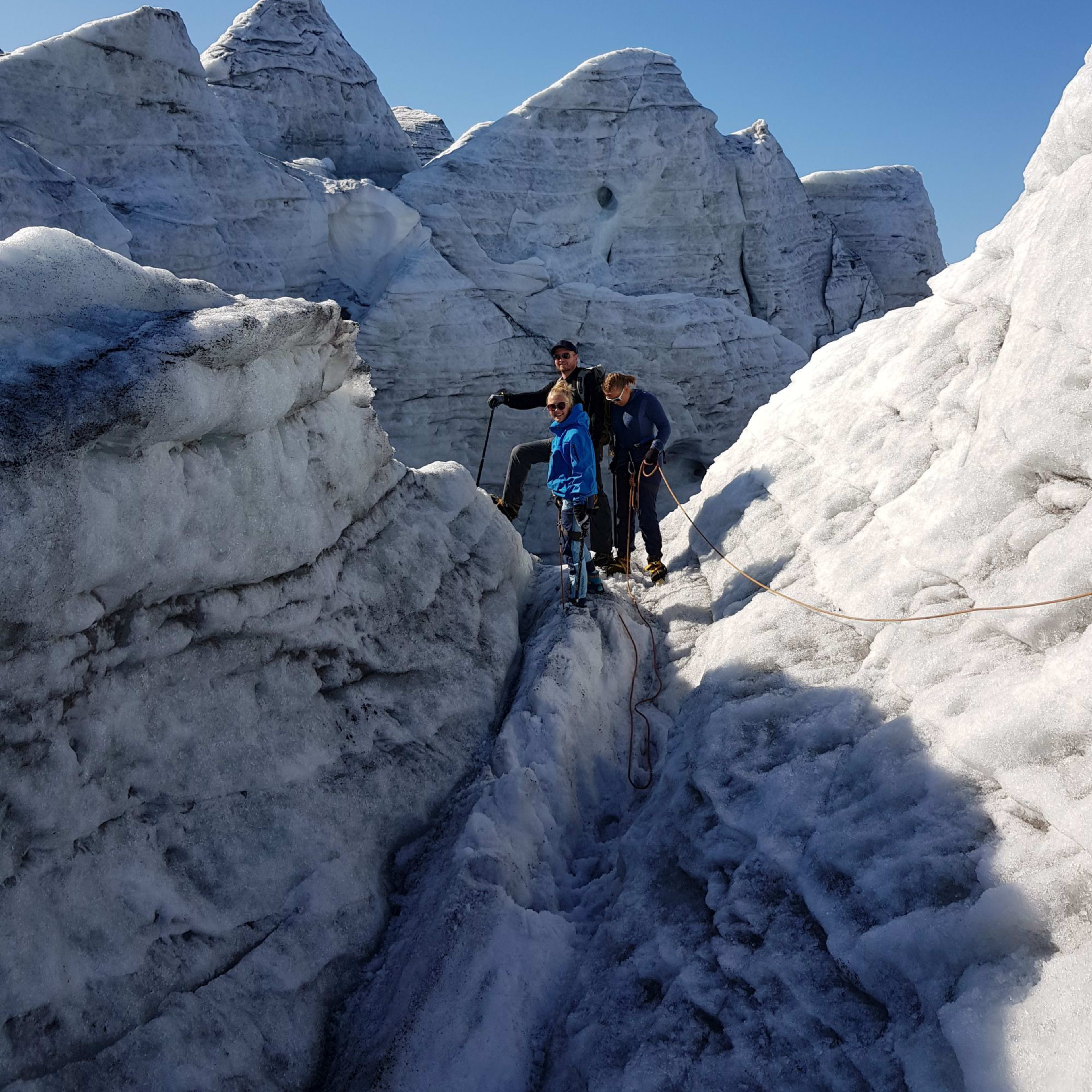 Tre klatrere står på breen, omringet av isformasjoner, klare for å takle det utfordrende terrenget.