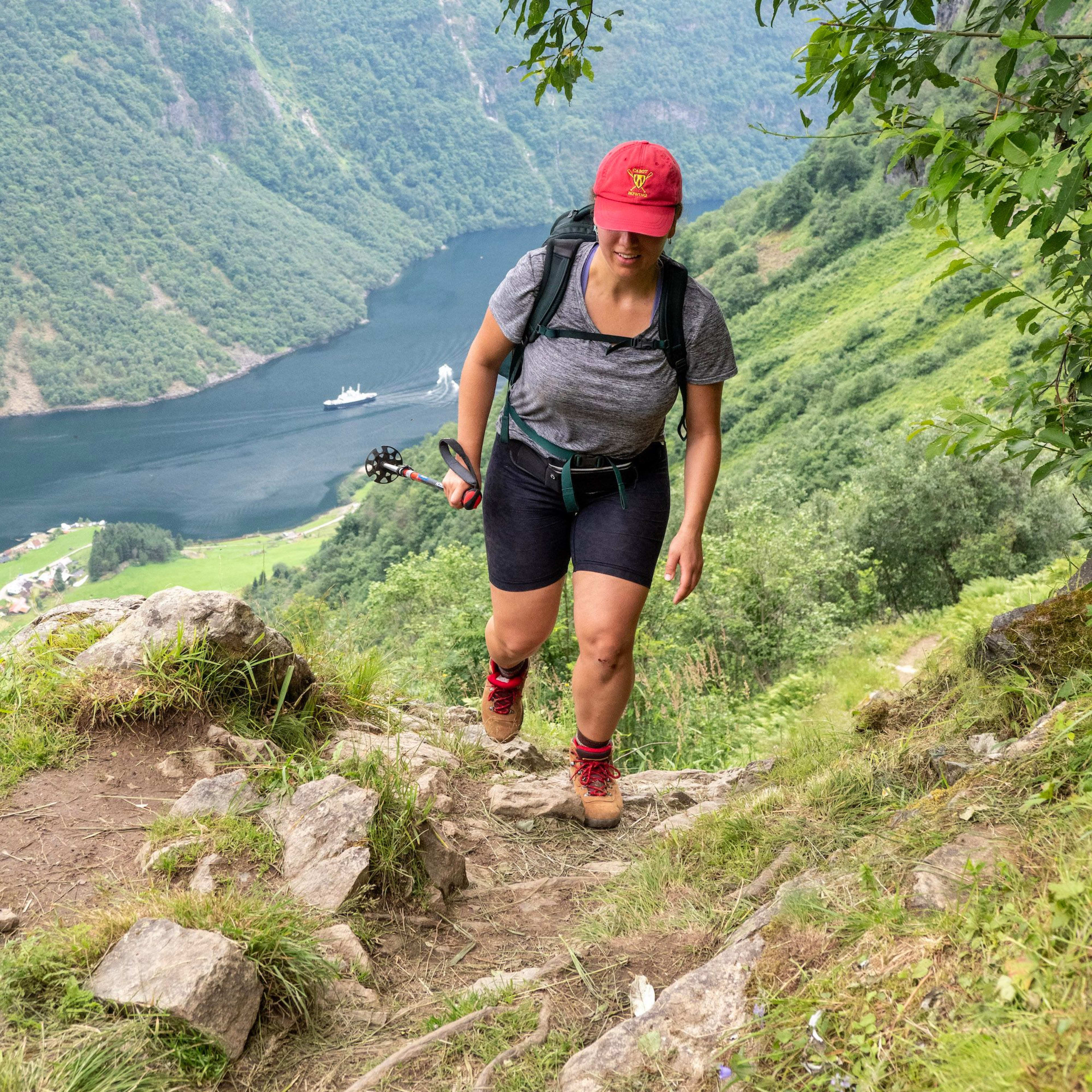 Woman climbing up on rock stairs with the fjord behind her, surrounded by green mountain hills.