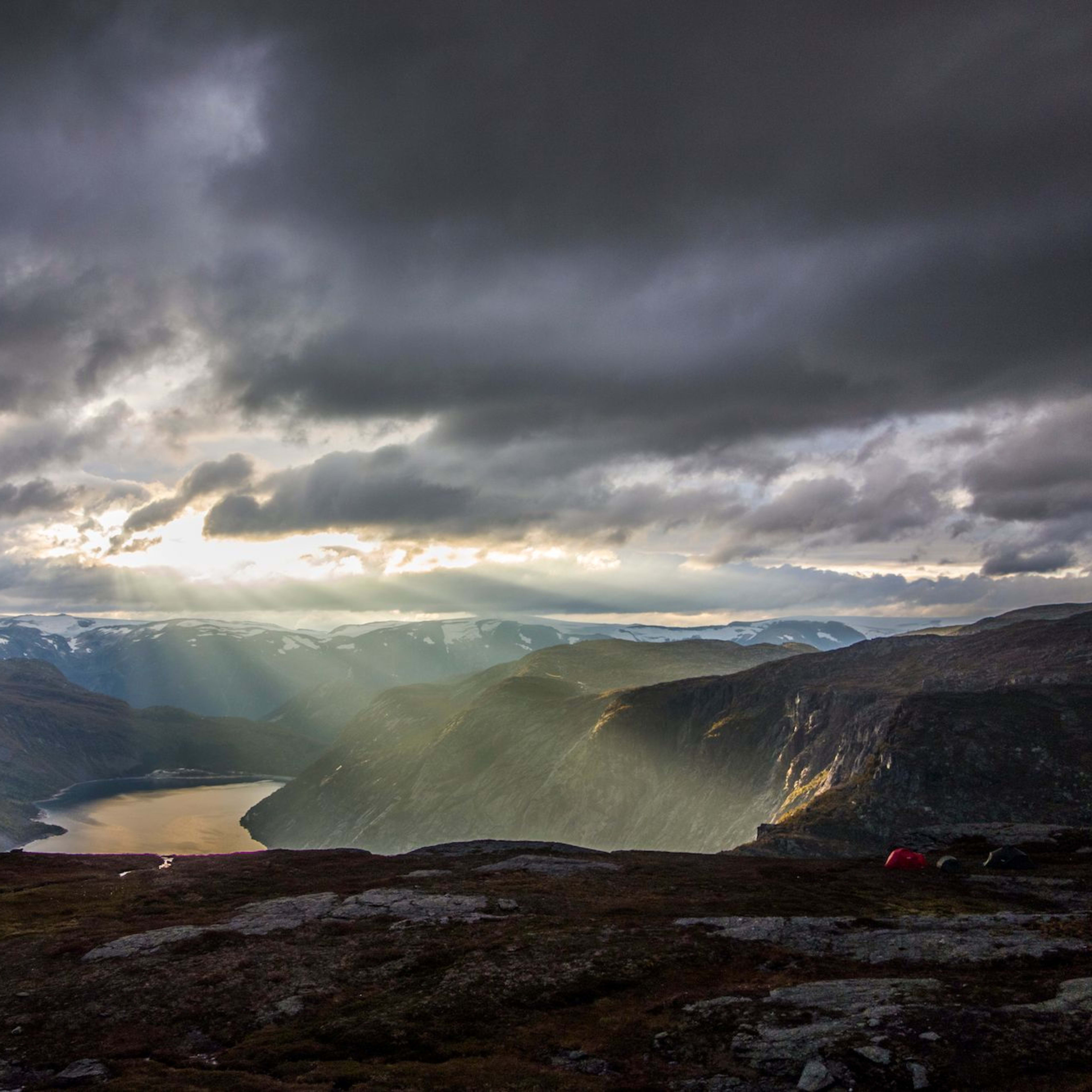 Dramatische Fjordlandschaft mit schneebedeckten Bergen und Sonnenstrahlen, die durch Wolken brechen.