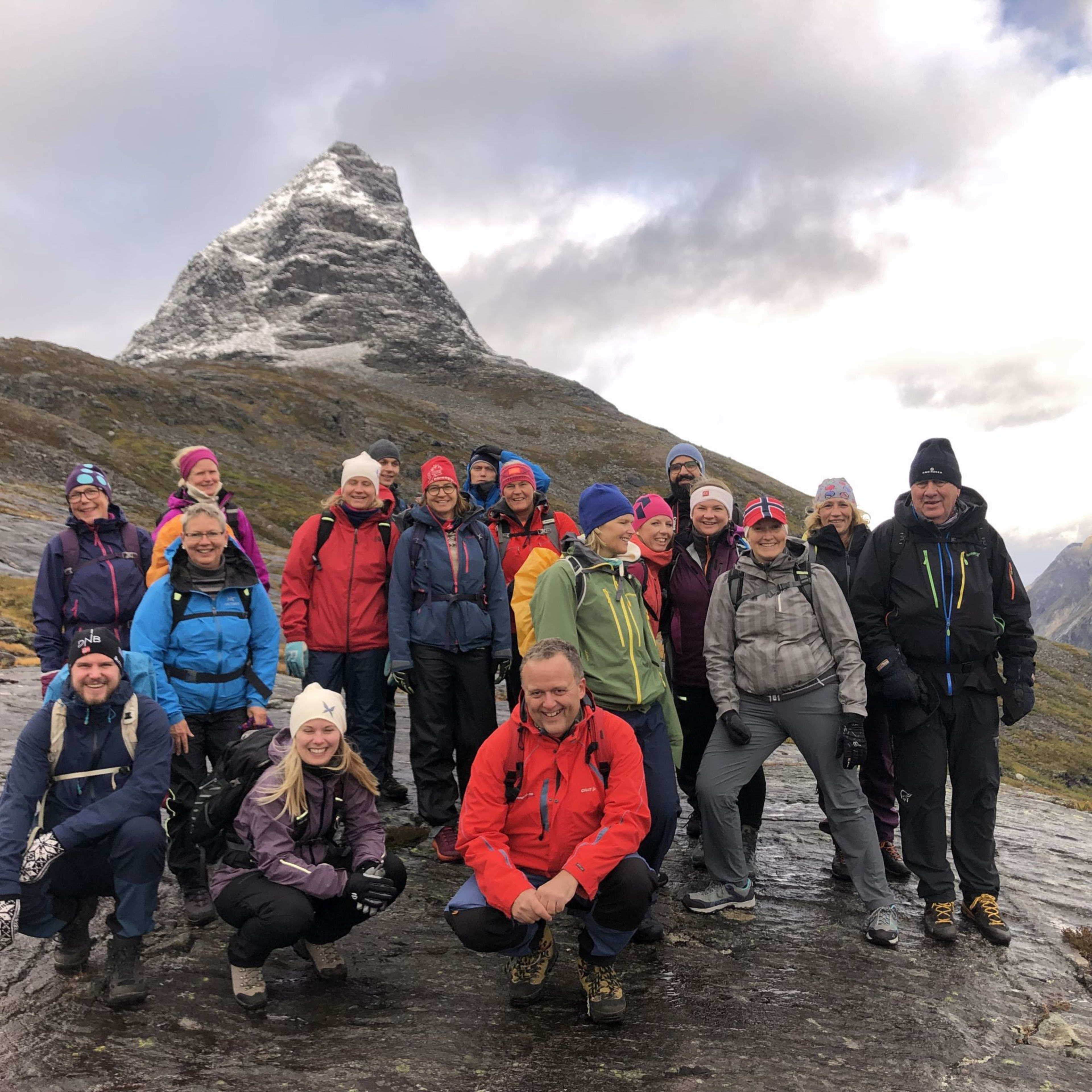 Eine Gruppe von Wanderern posiert für ein Foto auf rauem Terrain, mit einem schneebedeckten Berg im Hintergrund.