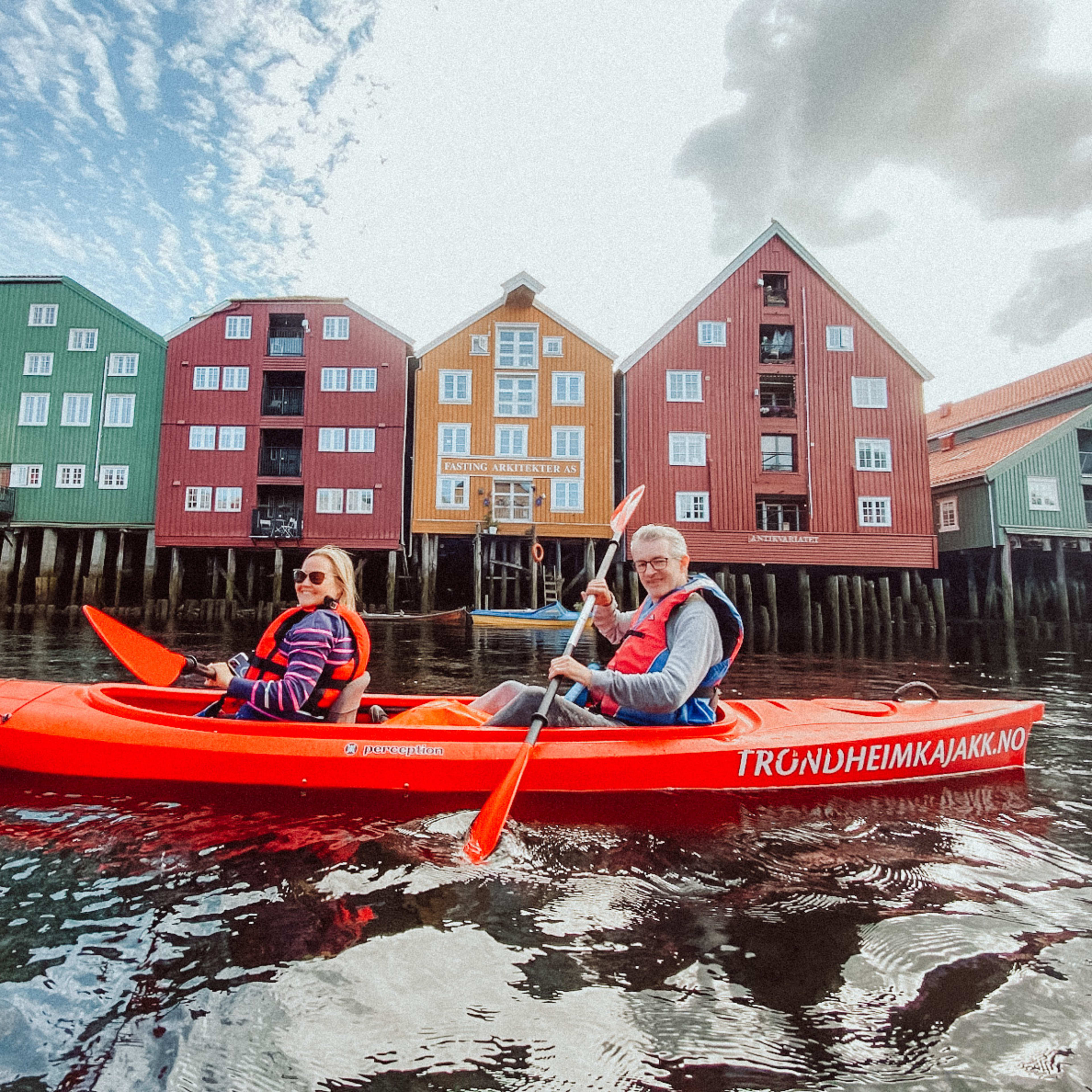 Par som padler kajakk forbi fargerike historiske bygninger i Trondheim på guidet sommertur med flotte utsikter langs Nidelva