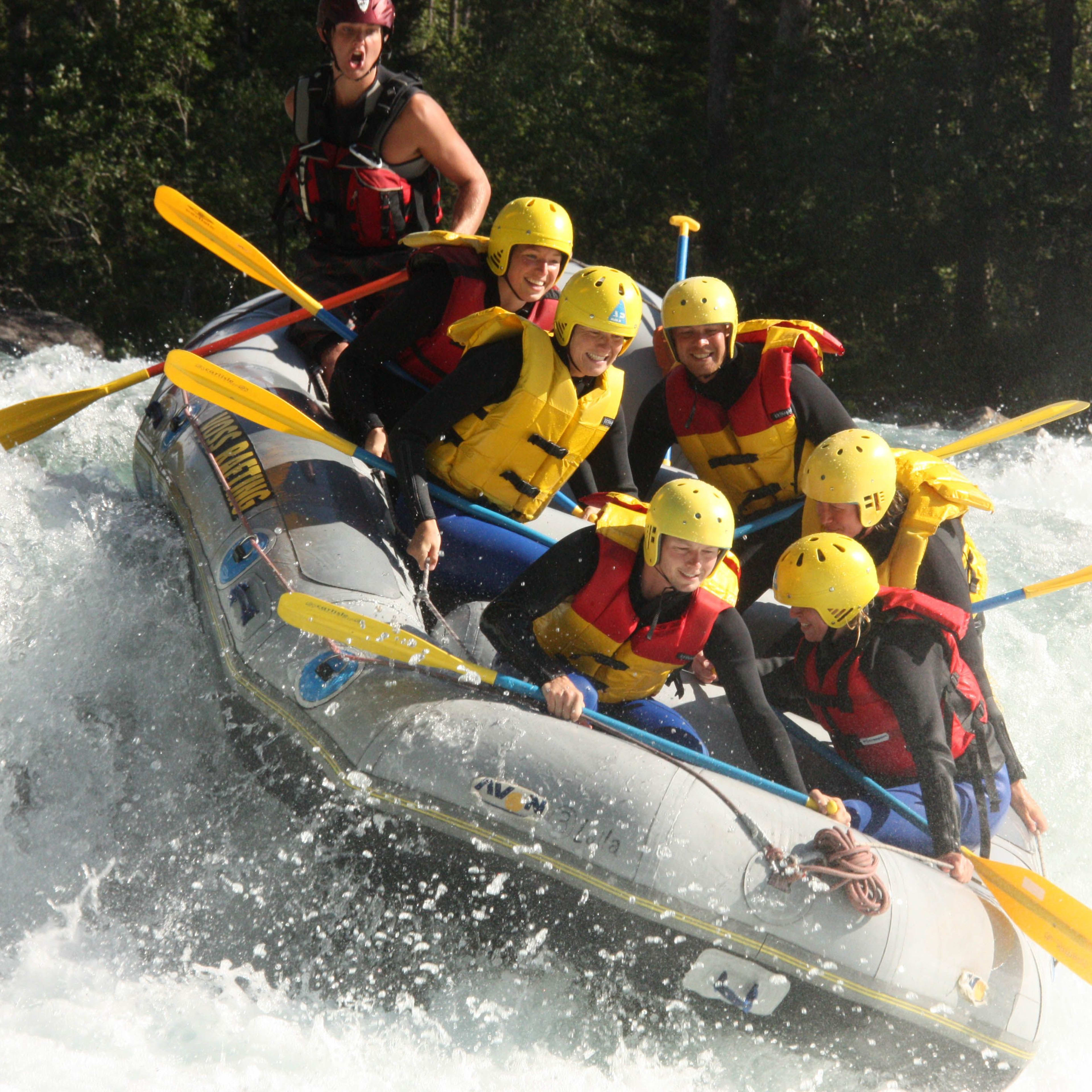 Eine Gruppe von sieben paddelt in einem gelben Raft durch Wildwasser, mit einem Guide, der von hinten steuert.