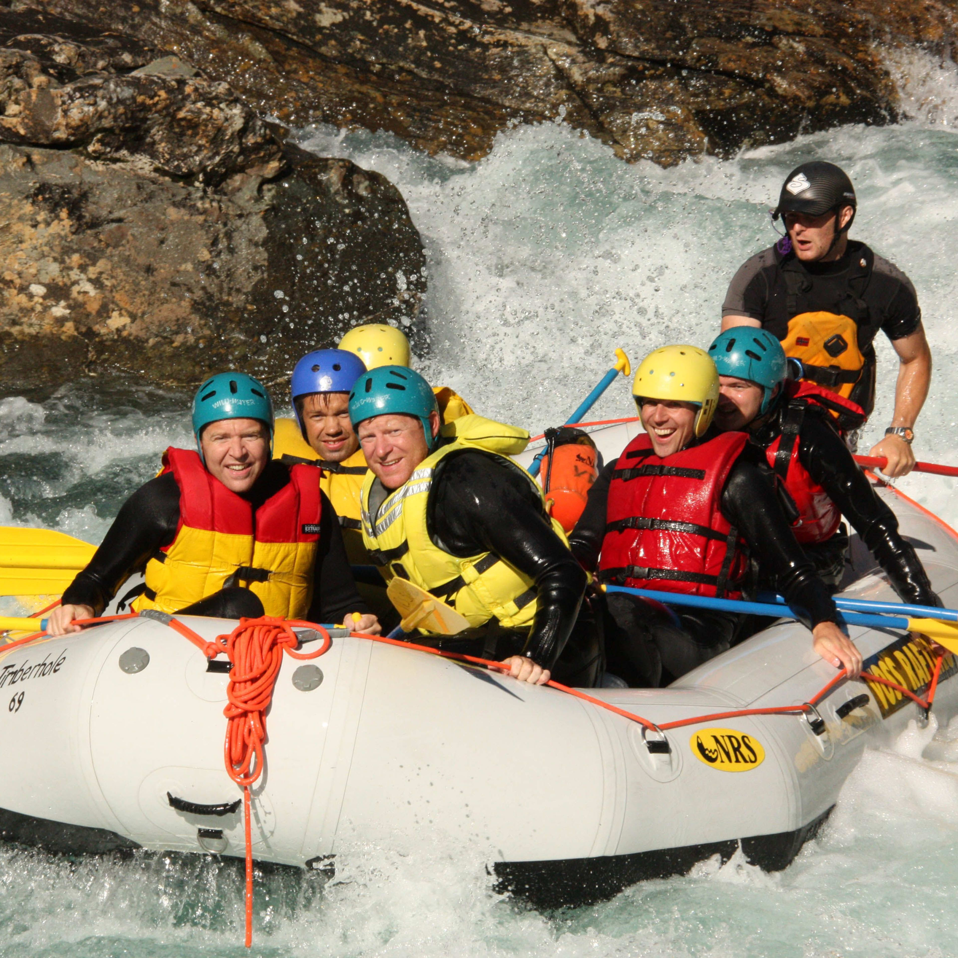 Eine Gruppe von Menschen genießt ein aufregendes Rafting-Erlebnis, paddelt durch schnell fließendes Wasser mit Wasserspritzern.