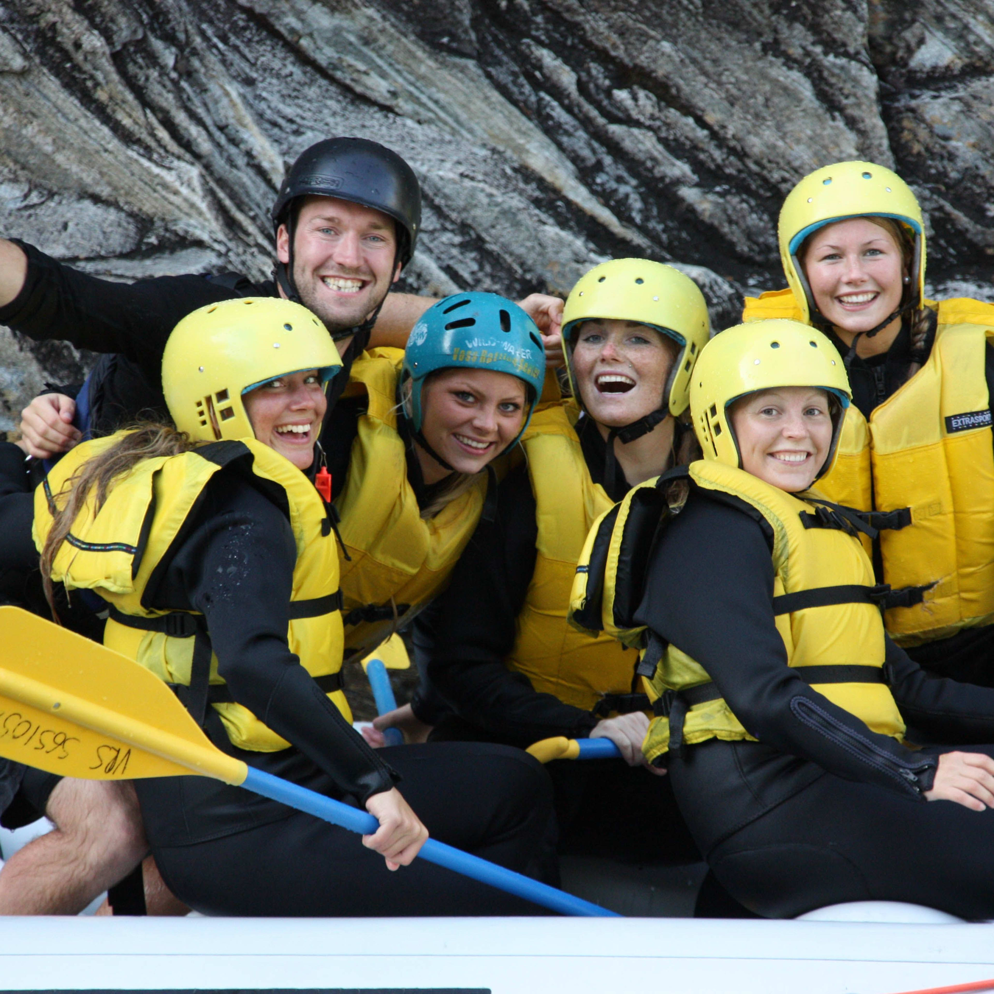 Eine Gruppe von sechs Personen lächelt und genießt das Rafting zusammen in einem Raft.