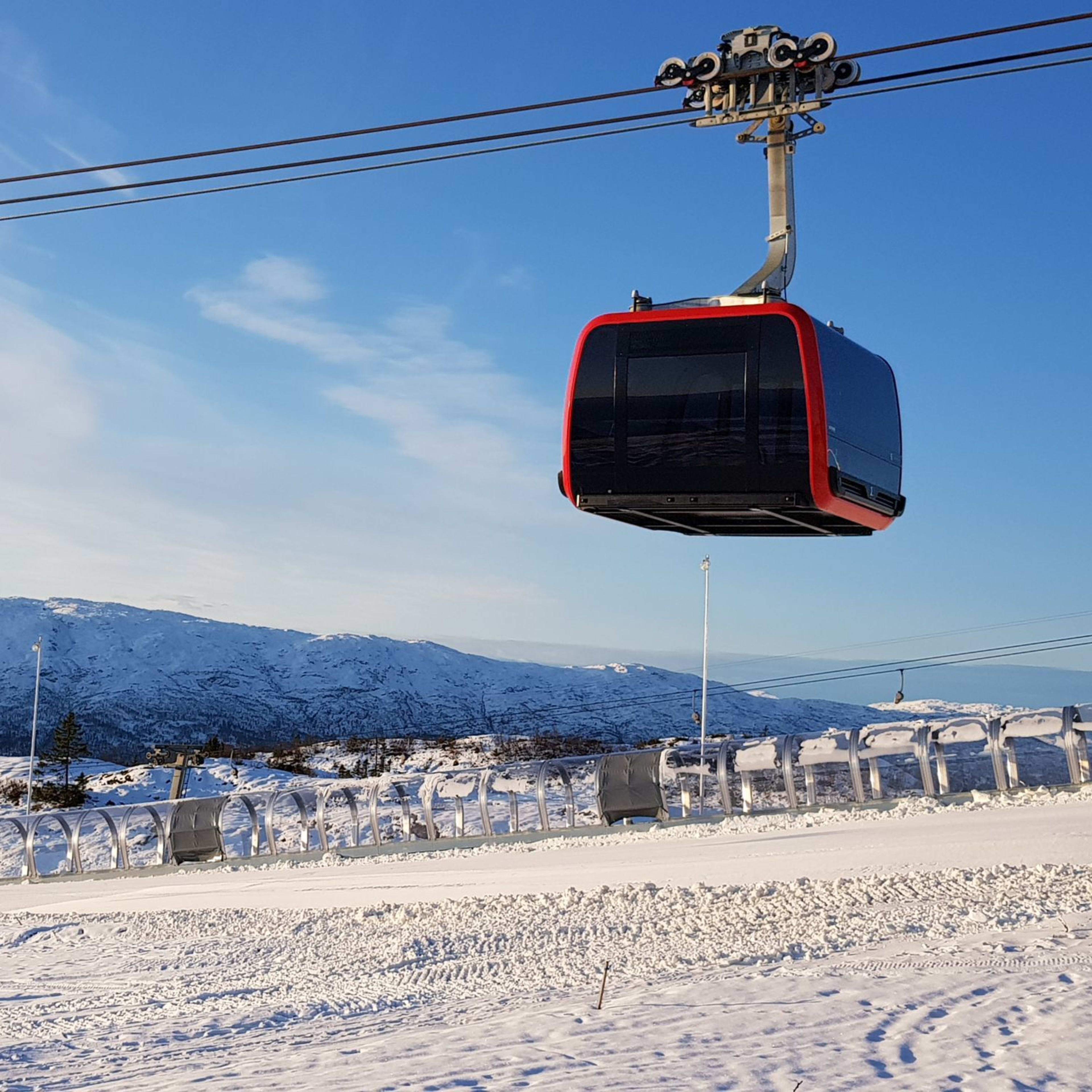 Rote Gondel über Piste mit Förderband und Bergen.