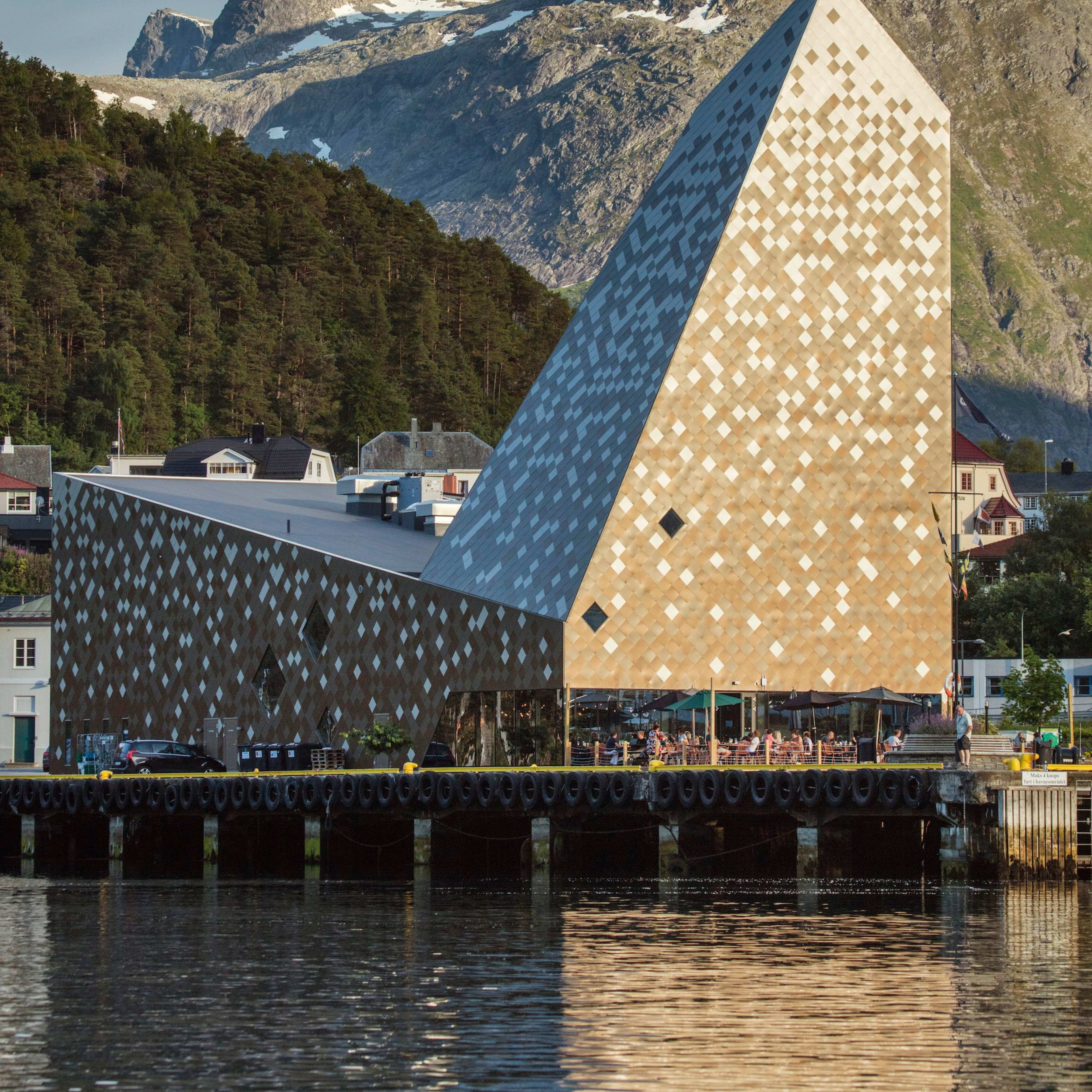 A modern architectural building with a geometric facade of beige and white tiles, located near a dock.