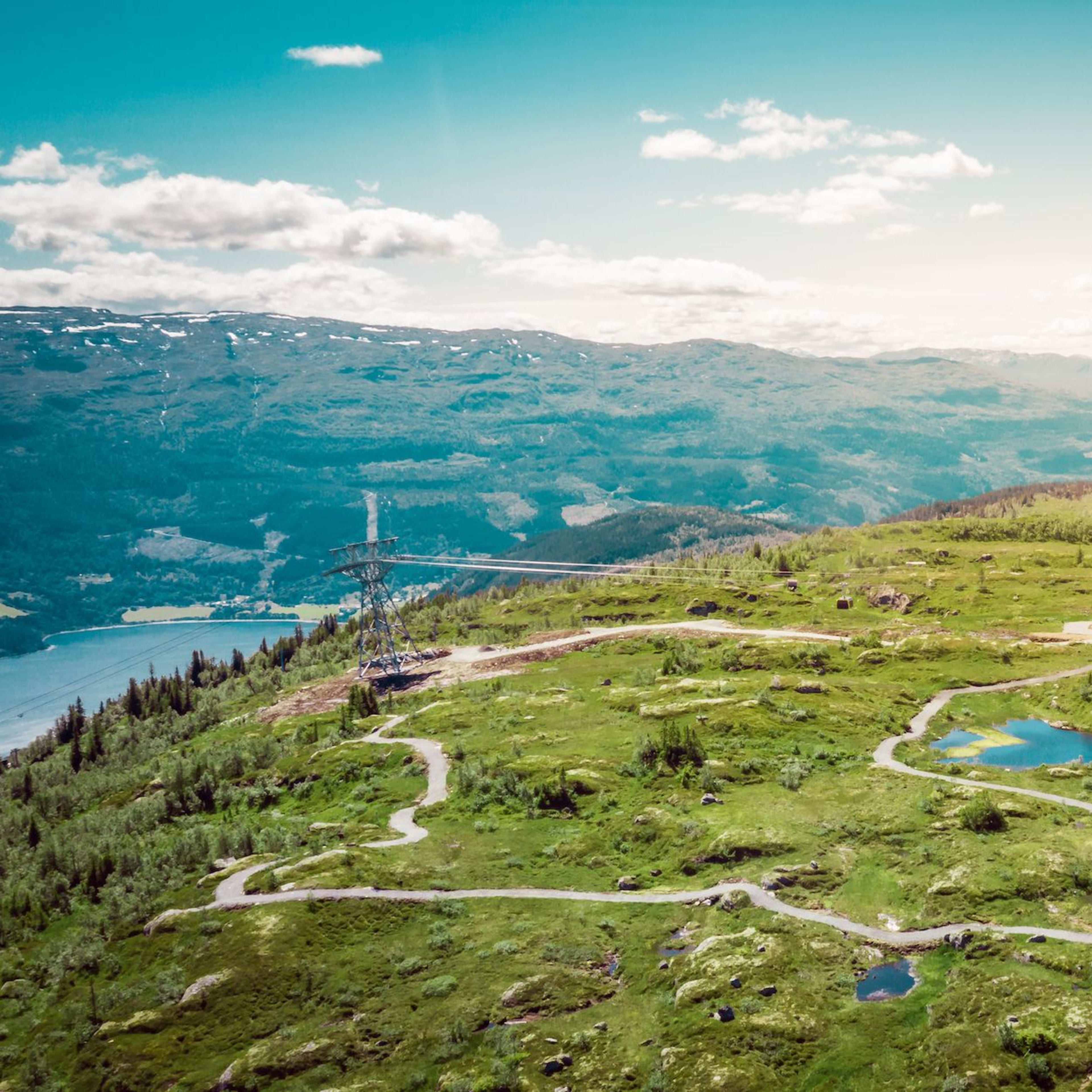 Mountaintop with trails, ponds, and cable car station overlooks a valley and mountain ridges.