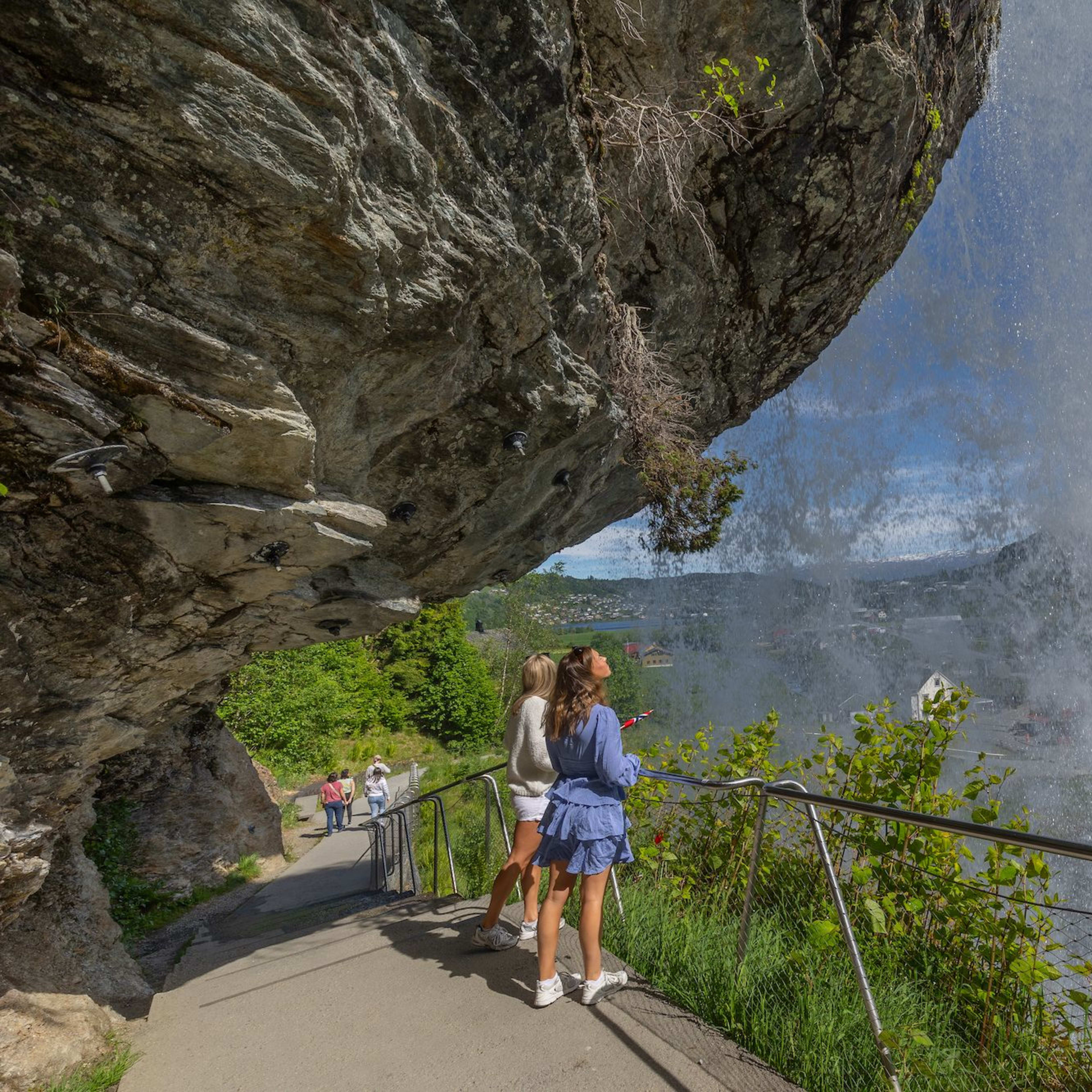 Zwei junge Frauen stehen sicher hinter dem Steinsdalsfossen und blicken durch den Wasservorhang