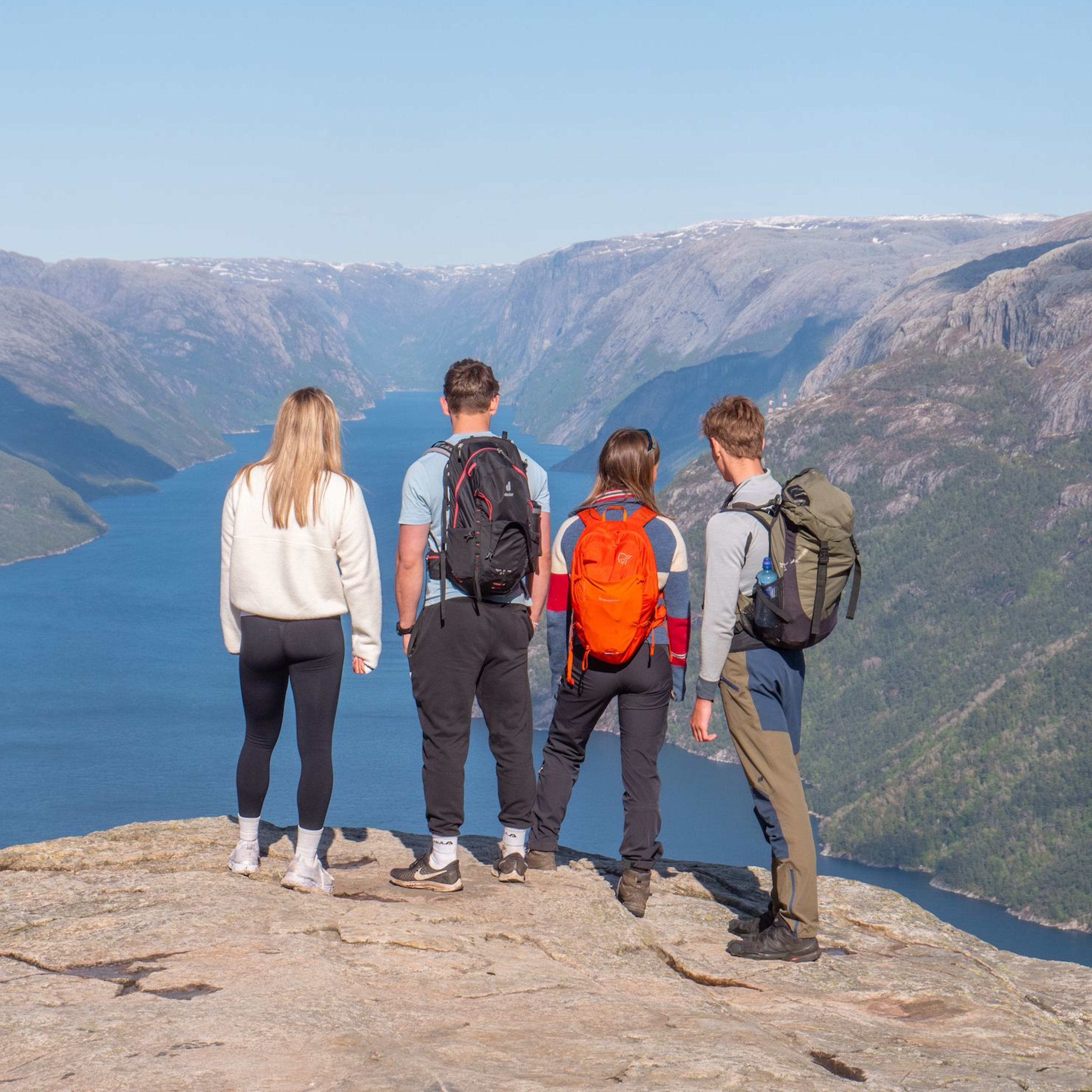 Hikers standing on the flat rock plateau of Preikestolen, taking in the breathtaking views of Lysefjord and the surrounding mountain landscape below