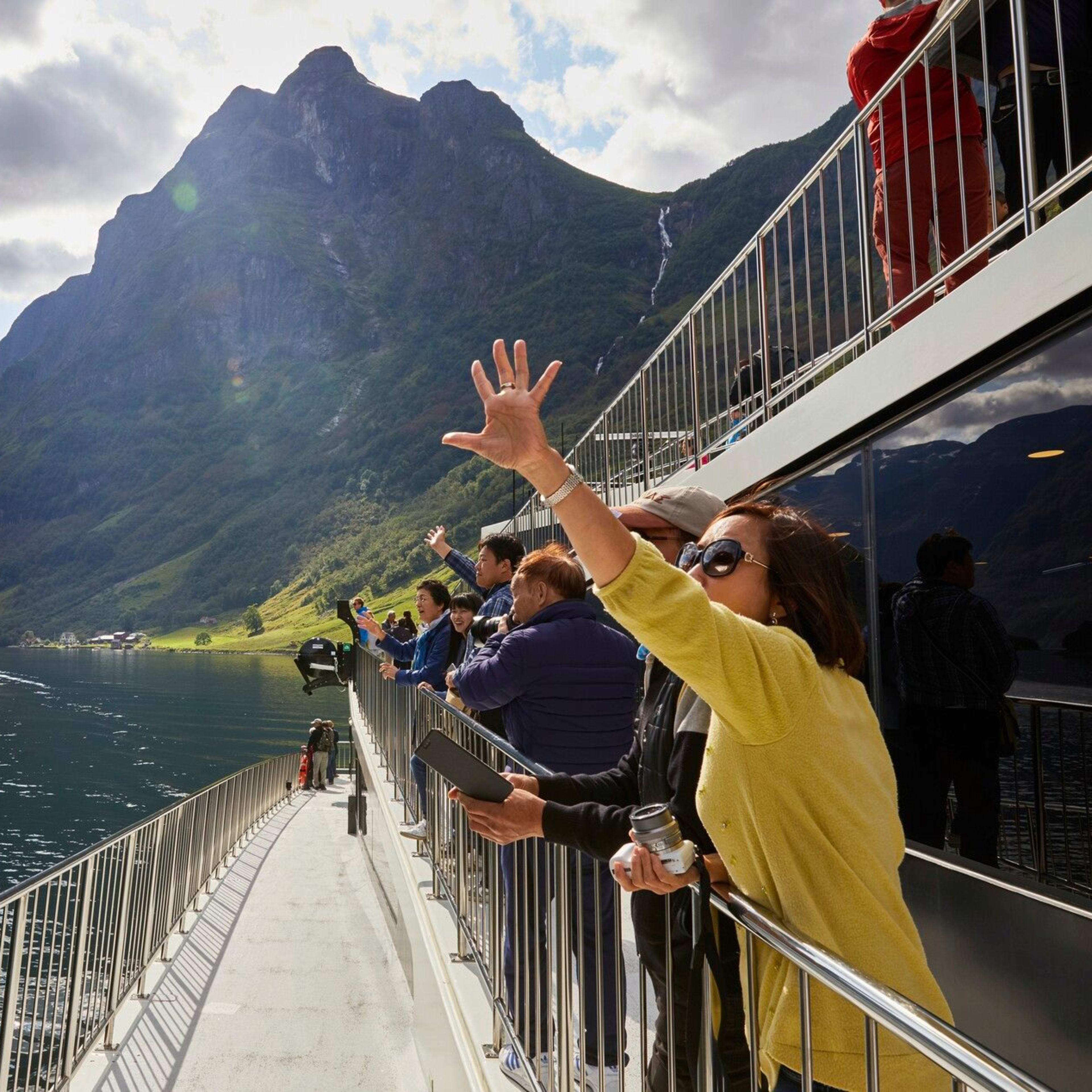 Passagiere winken und fotografieren bei Fjordfahrt am Nærøyfjord.