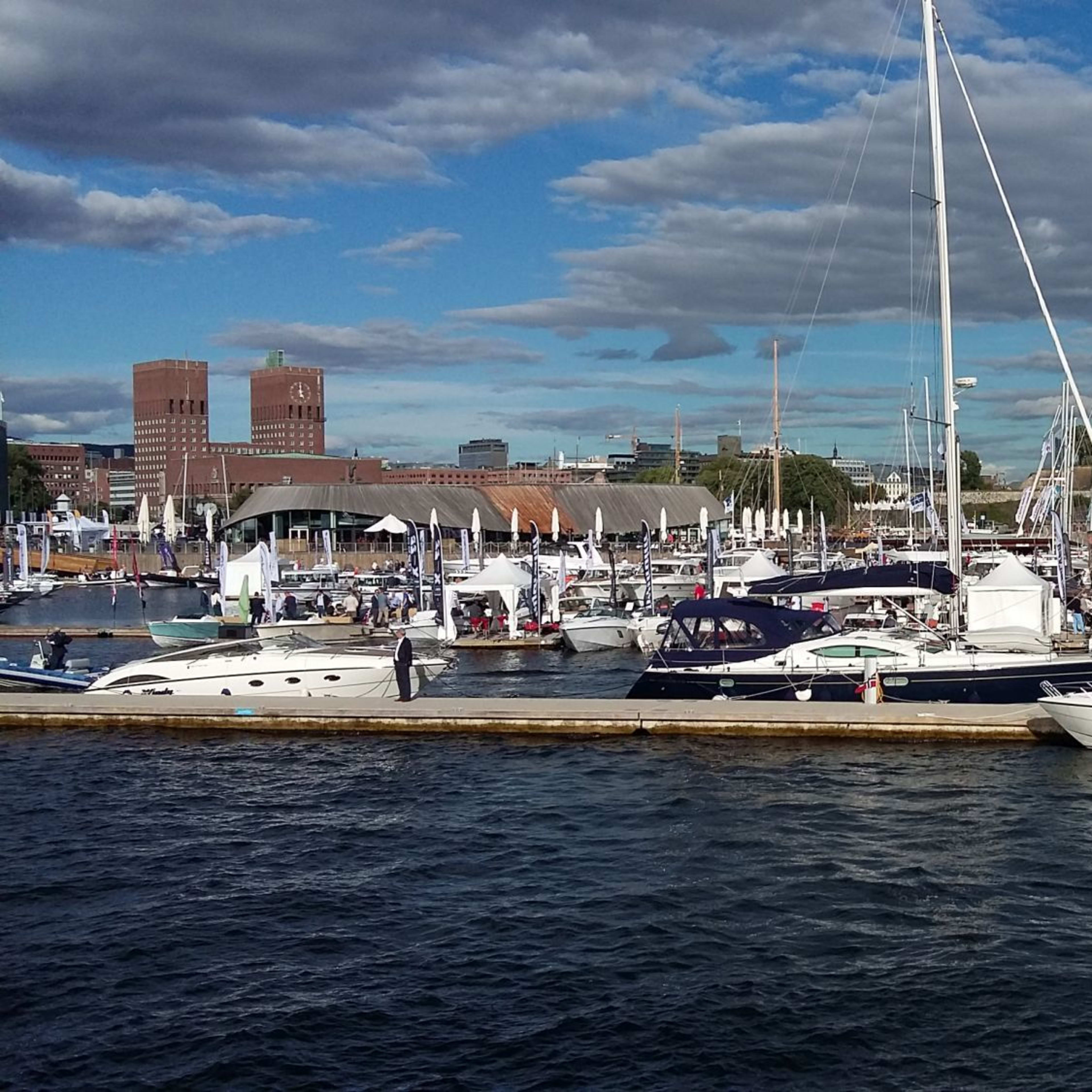 Travel marina i Oslo med Rådhuset og båter under solrik himmel.