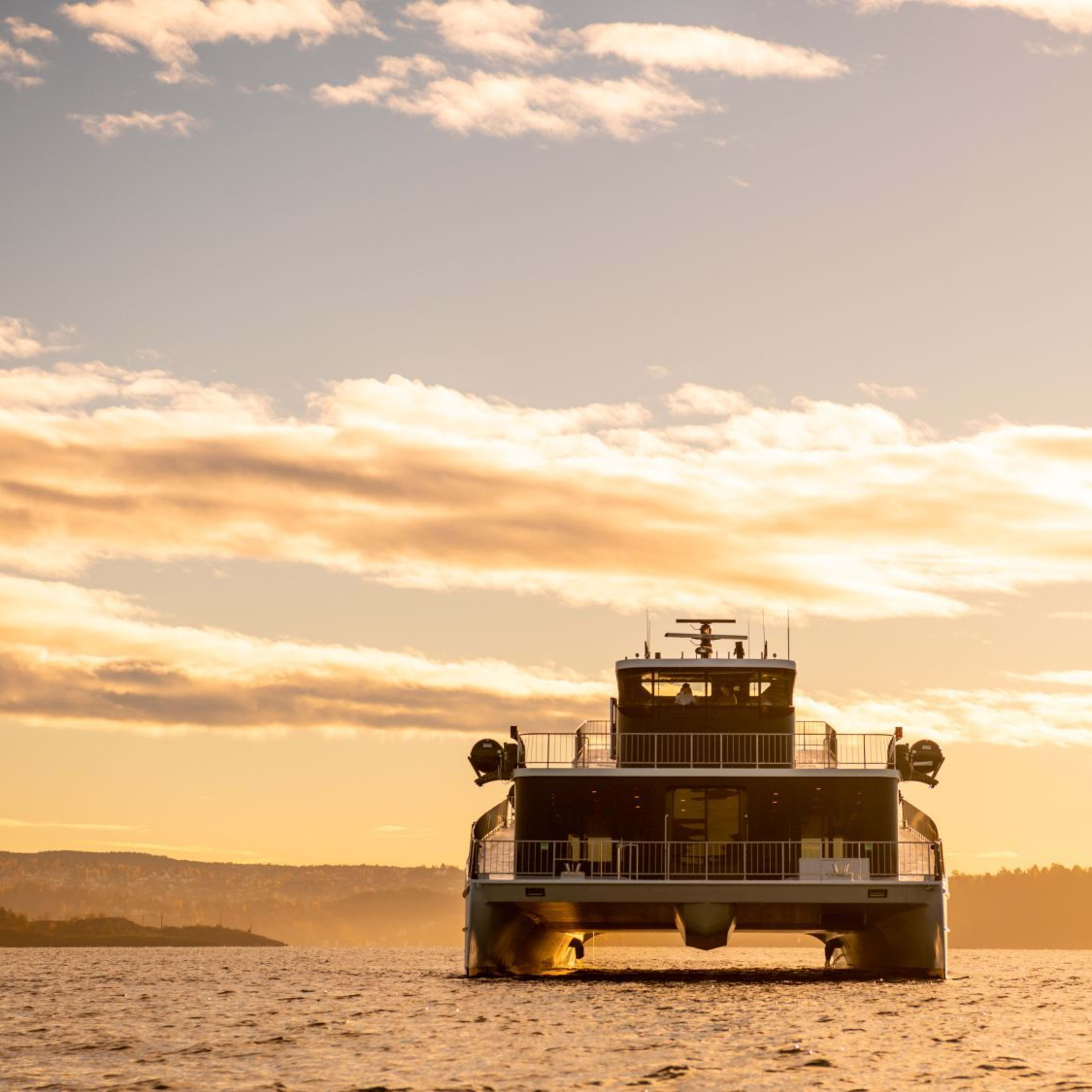 Rear view of ferry at sunset with warm sky colors and faint coastline in distance.