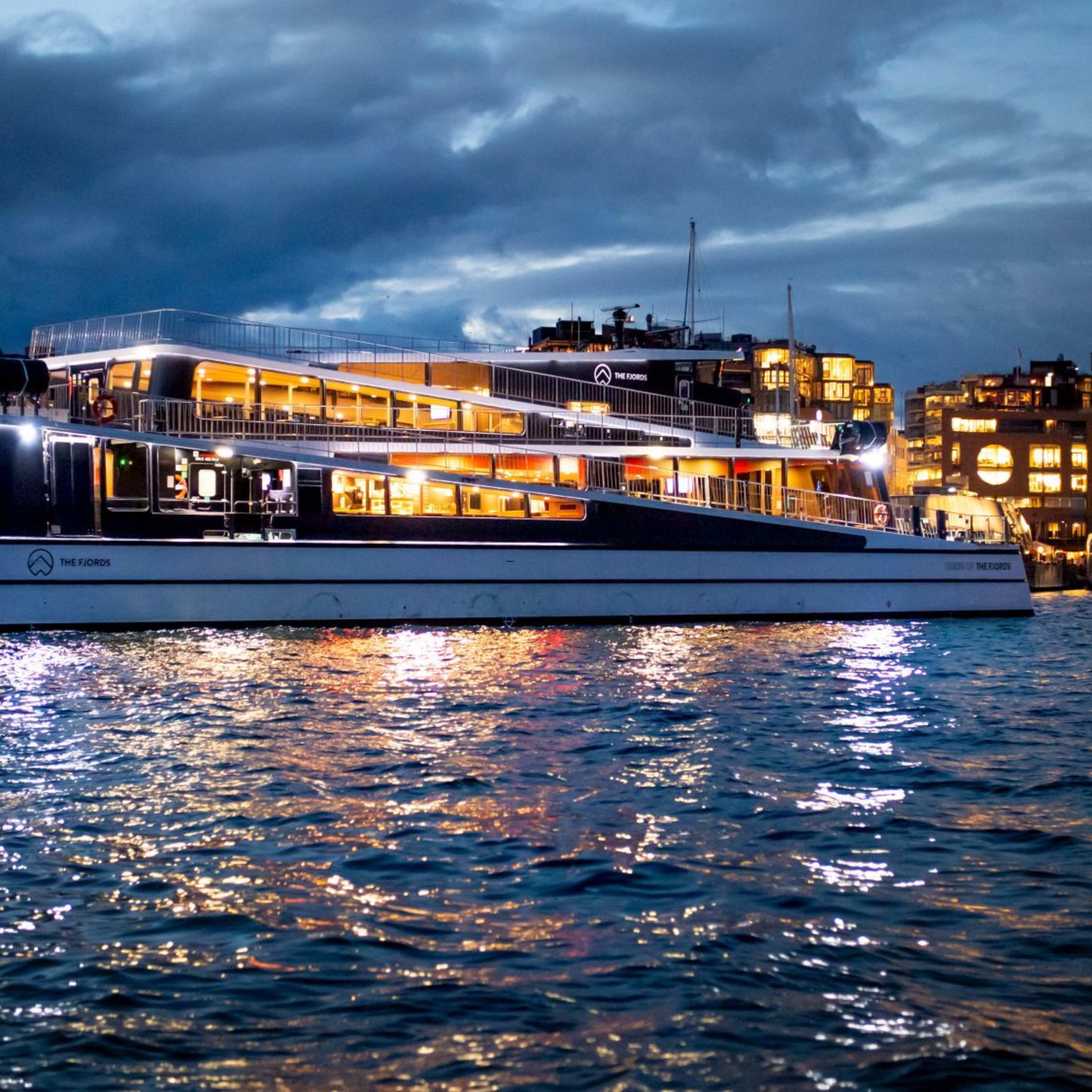 Illuminated ferry moves through night water with city lights and reflections creating contrast.