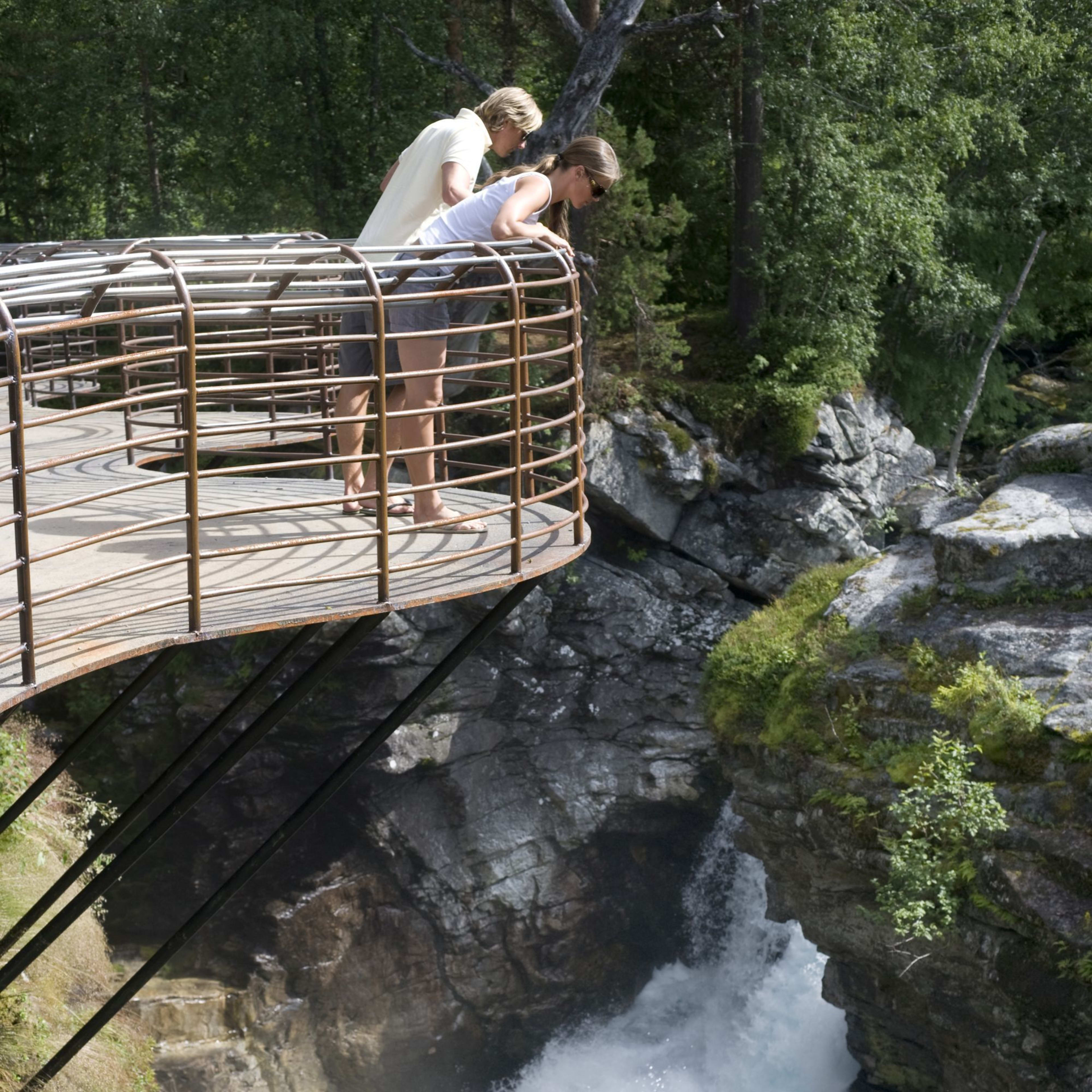 Two people lean over curved platform above narrow waterfall in Gudbrandsjuvet gorge.