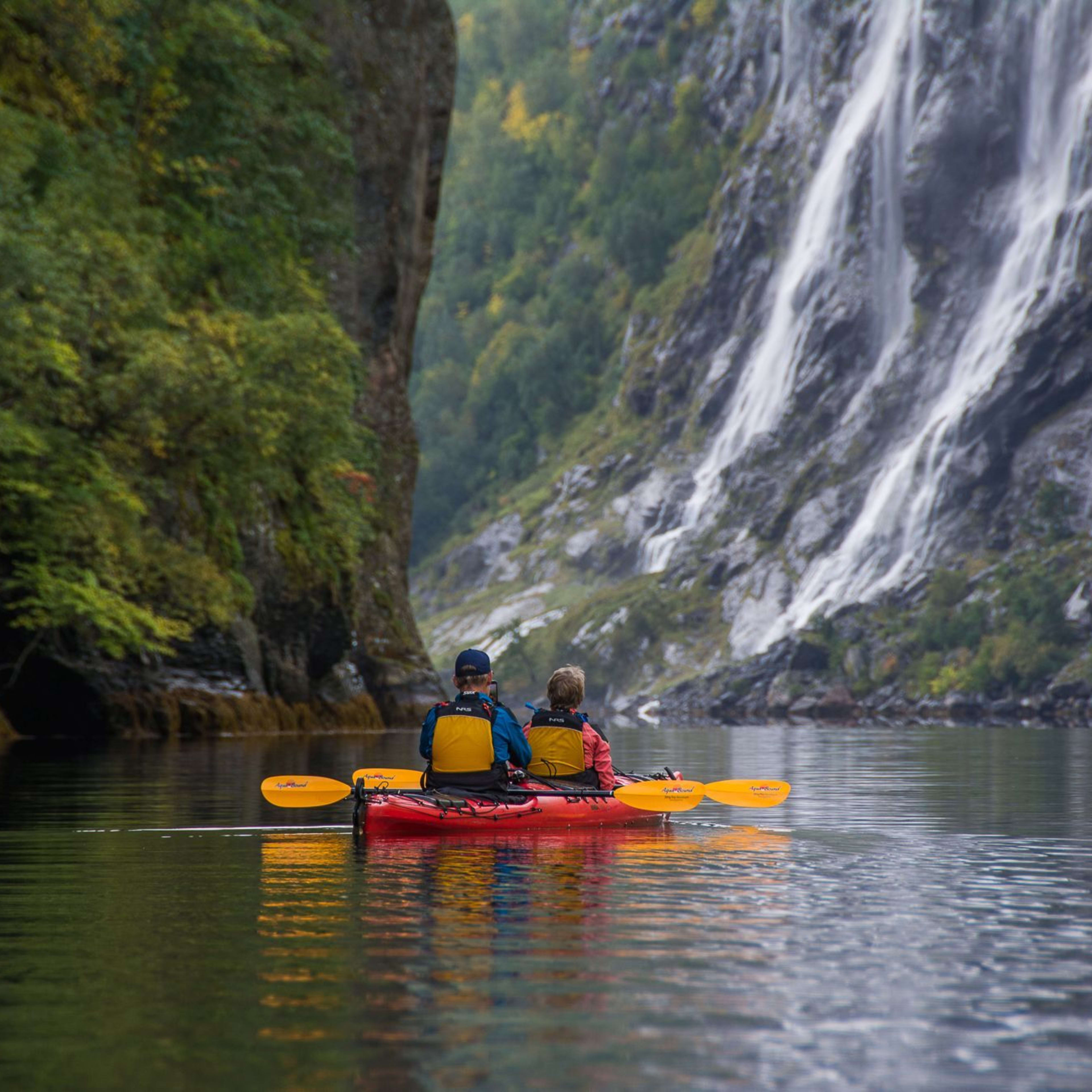 To personer i kajakk nær foss i fjord.