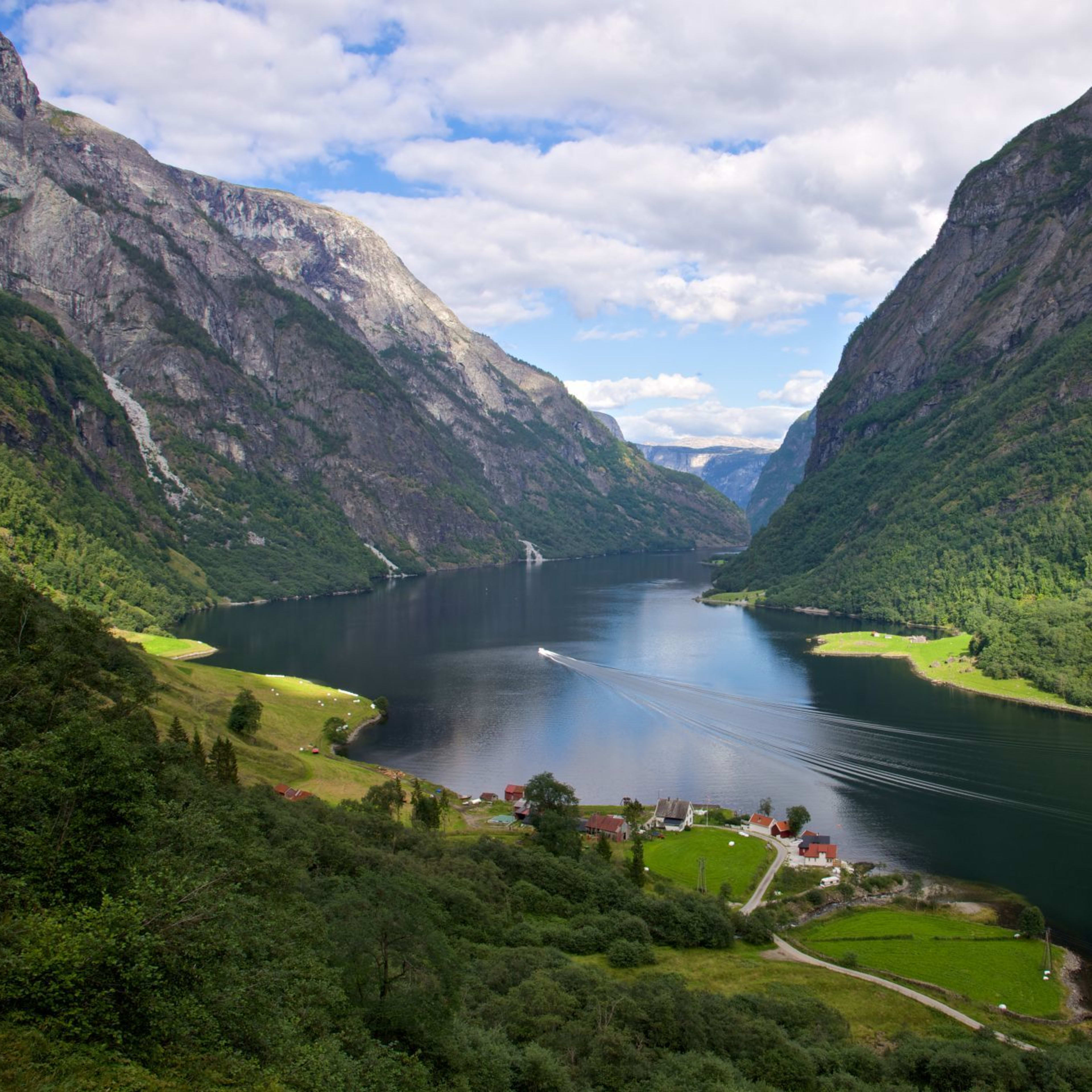 Smal fjord med båt og landsby ved vannet.