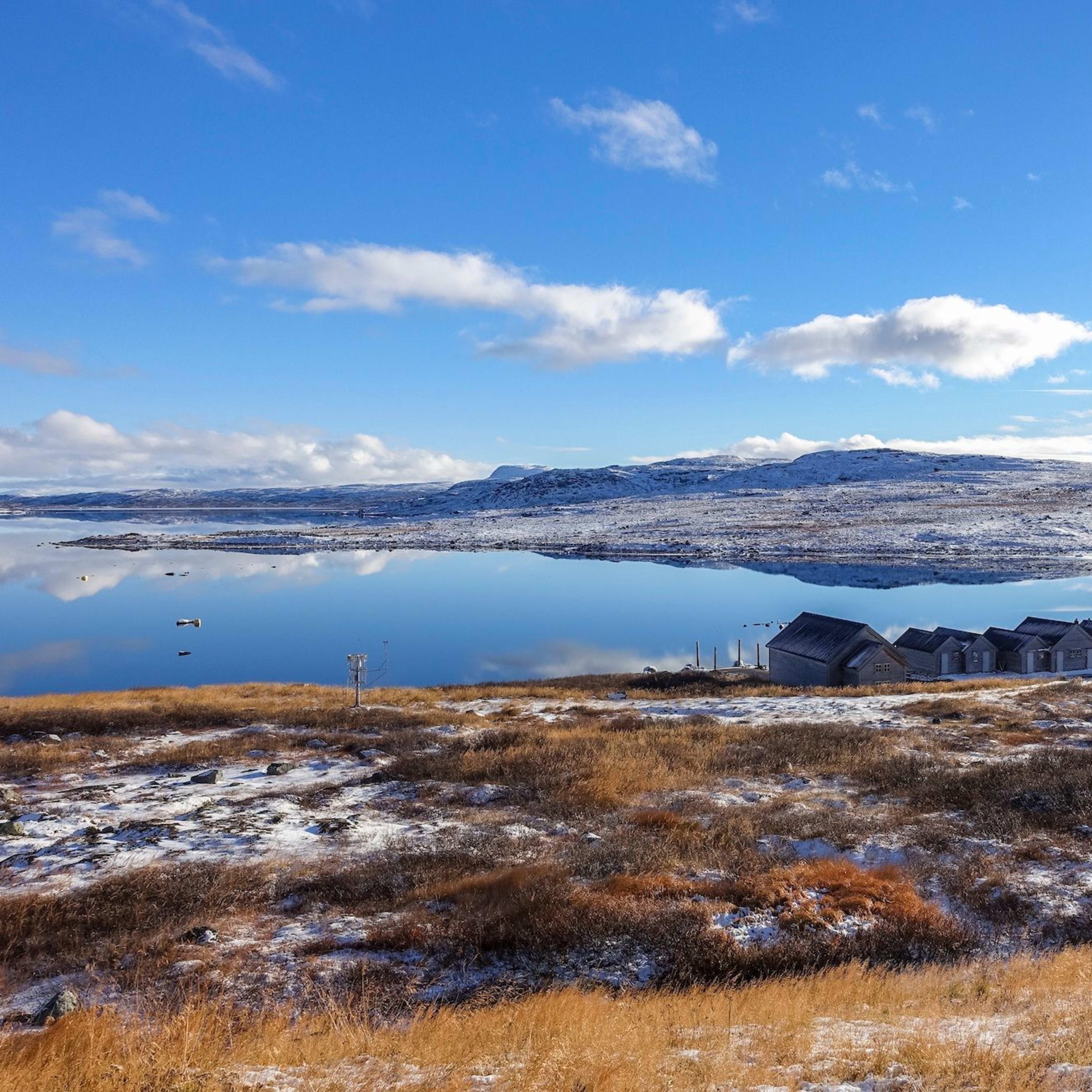 Holzhütten am See im verschneiten Gebirge unter blauem Himmel.