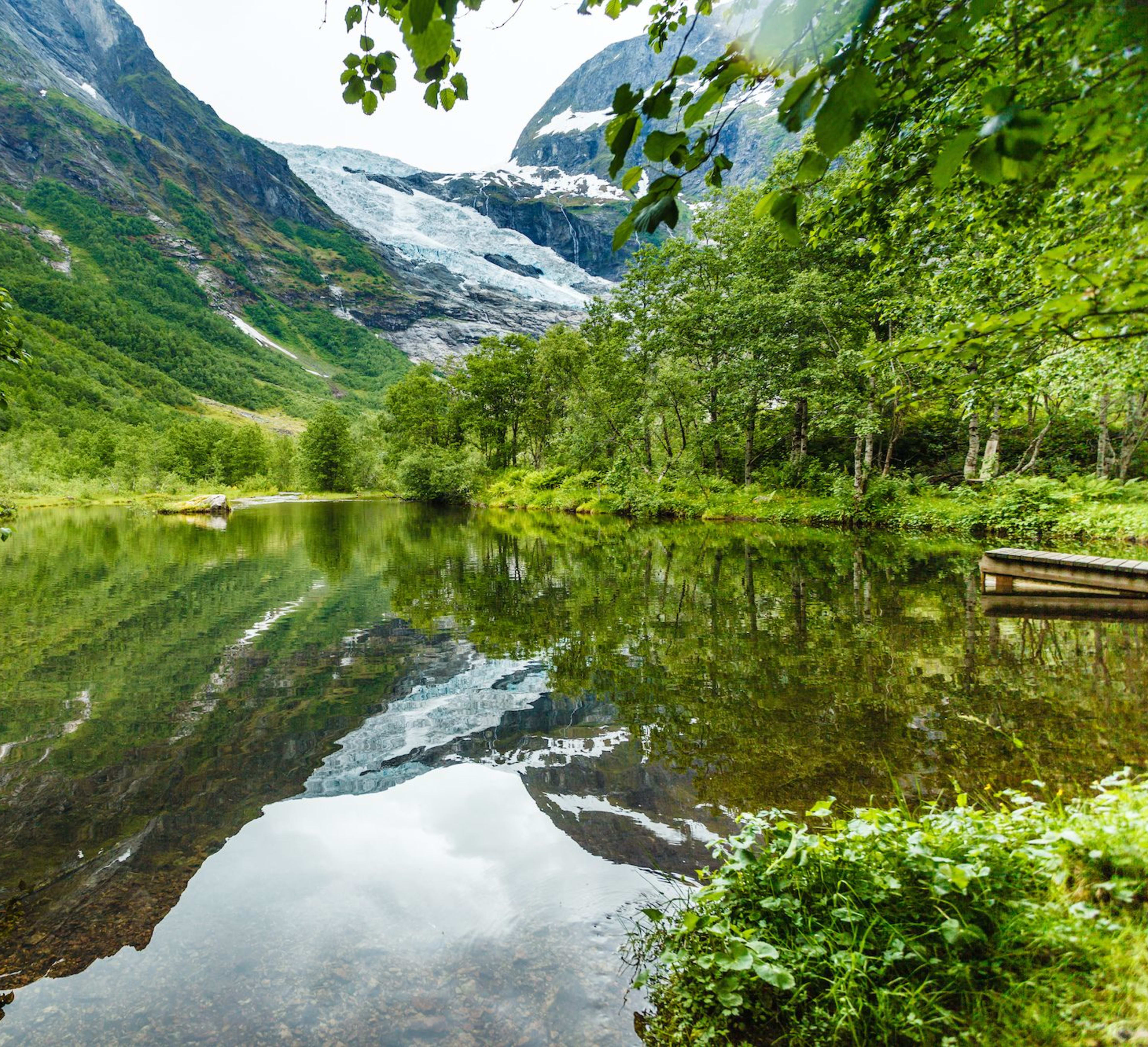 Snow-capped mountains reflect on a still lake by a wooden dock.