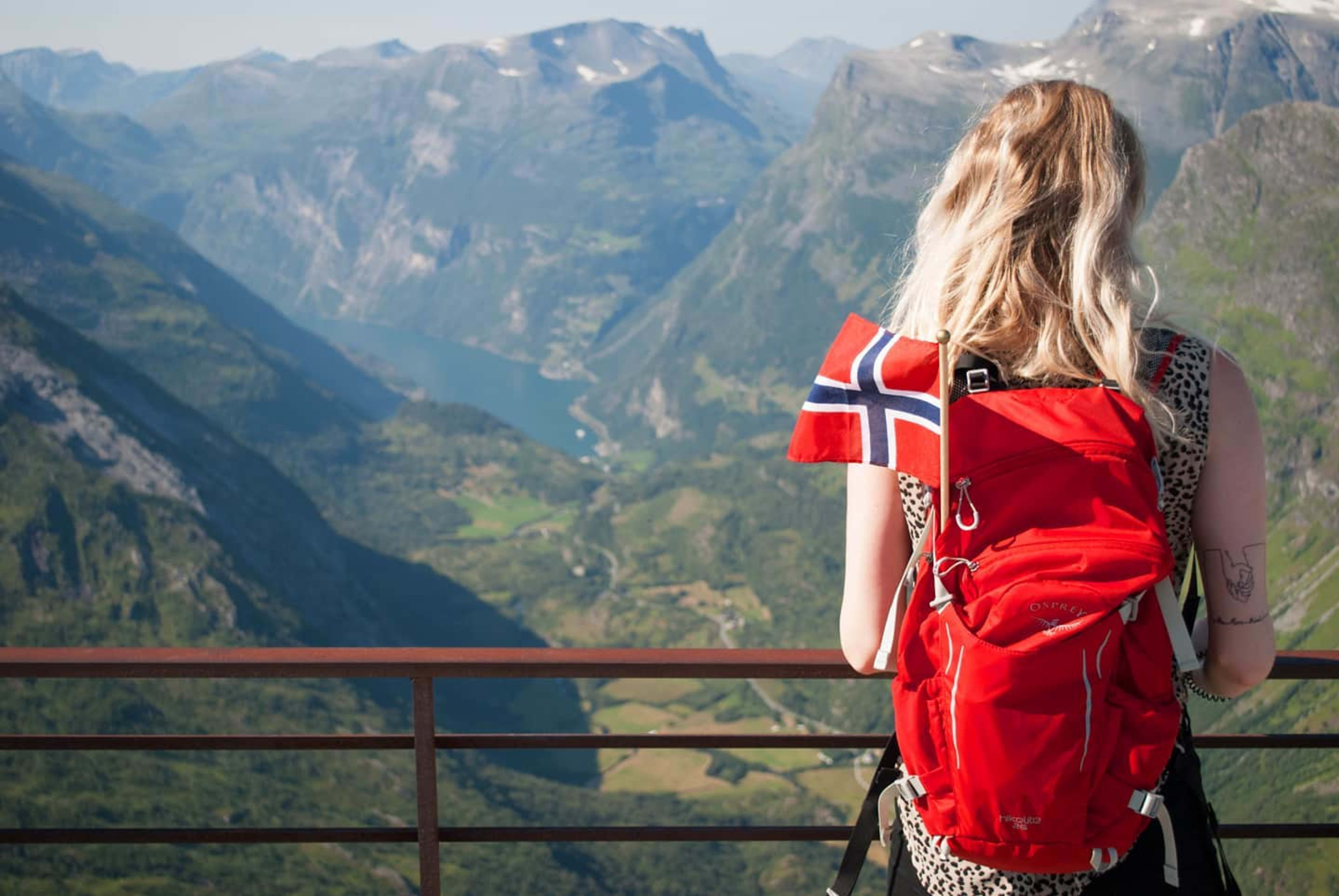 Jente som overser Geiranger og Geirangerfjorden med et norsk flagg i sekken