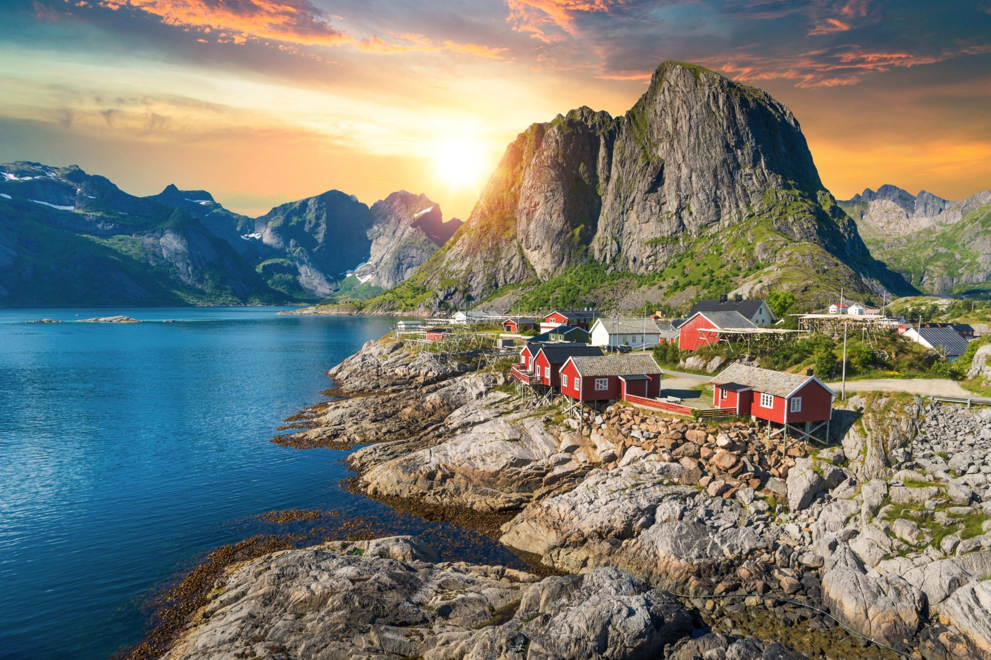 Sonnenuntergang über Fjord mit roten Hütten, Bergen und ruhigem Meer.