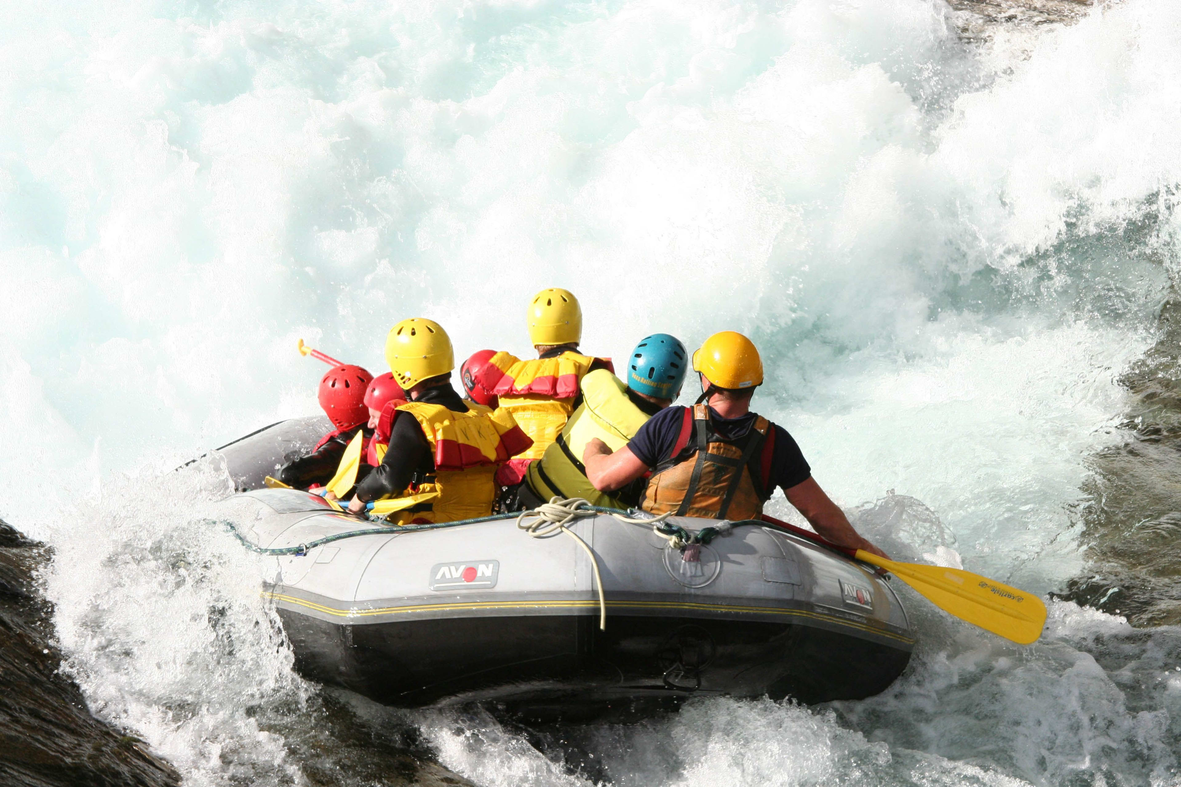 Eine Gruppe in einem kleinen aufblasbaren Raft navigiert durch turbulentes Wasser, mit kräftigen Wellen, die um sie herum brechen.
