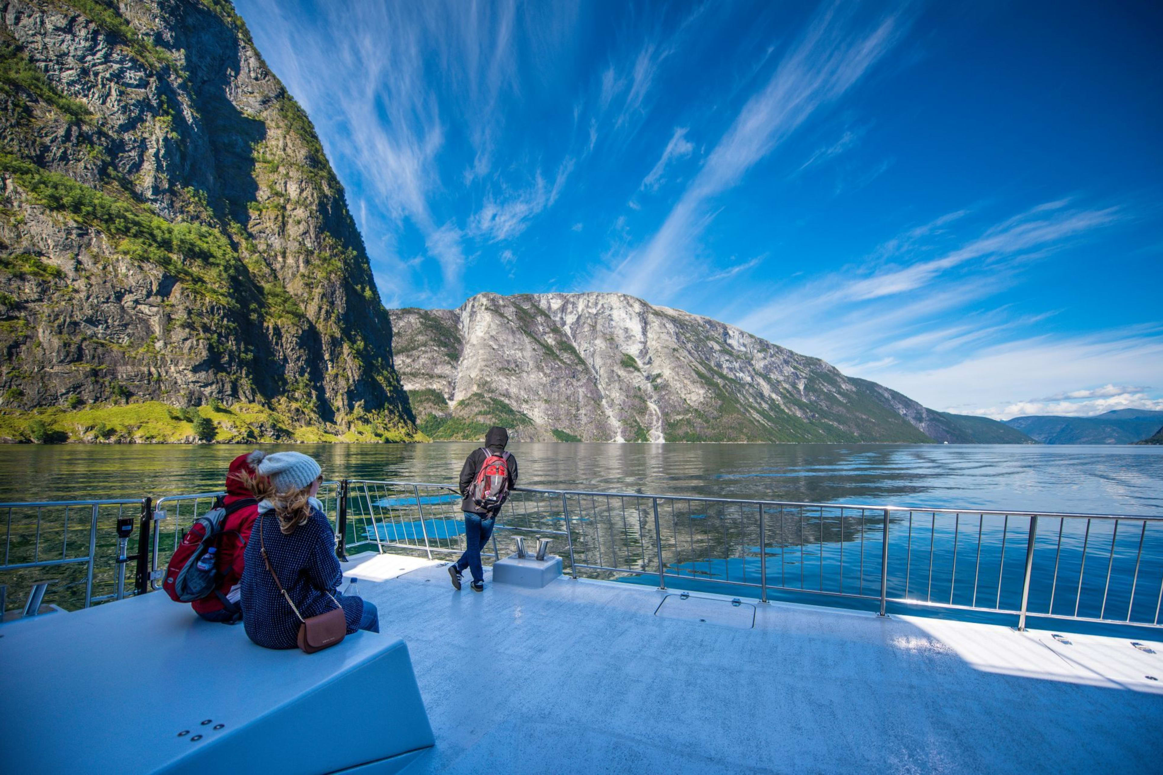 Menschen genießen Bootsfahrt durch Nærøyfjord mit Felsen, Grün und Schleierwolken.