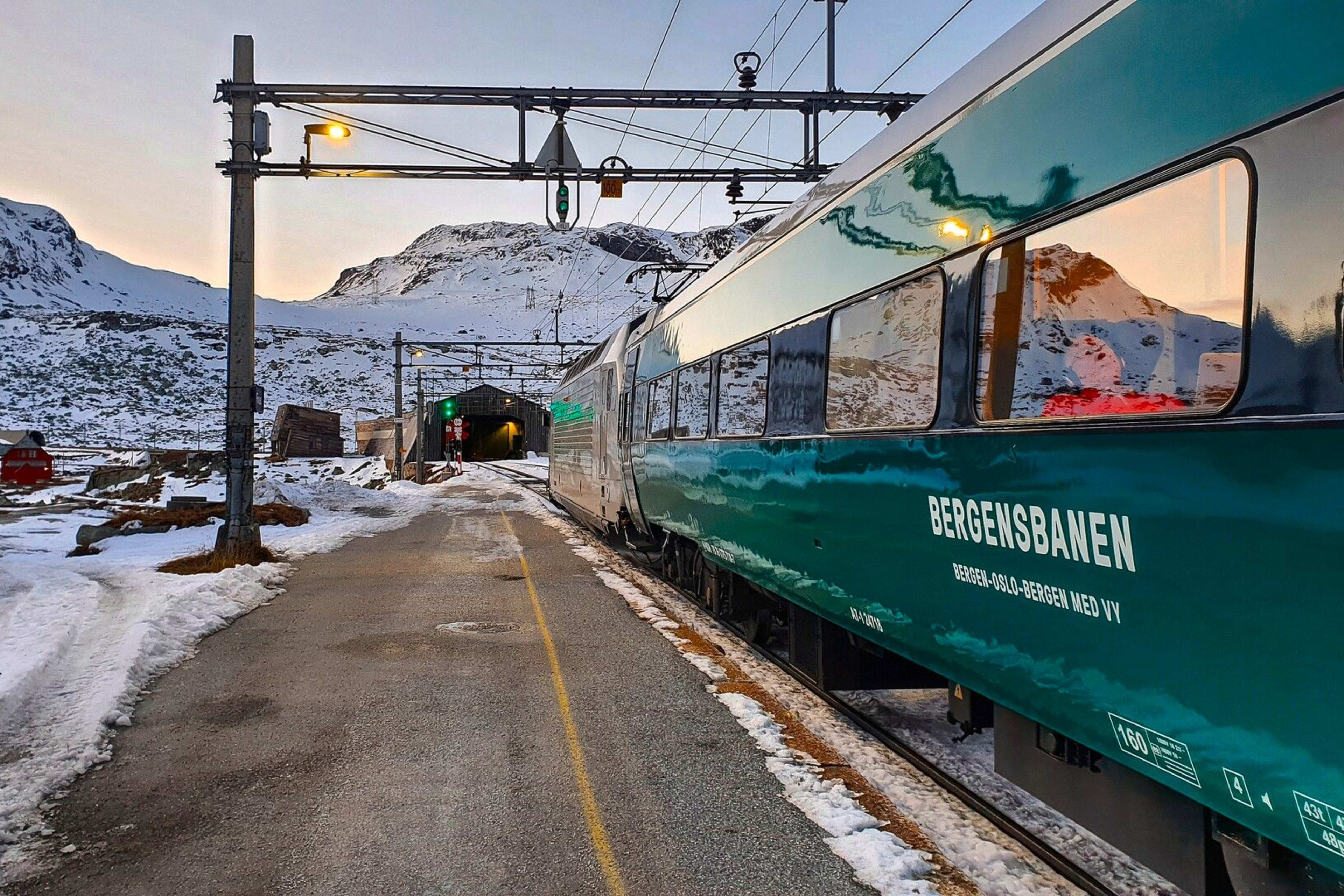 Nahaufnahme vom Bergensbanen-Zug, der durch malerische, verschneite Berglandschaft fährt.