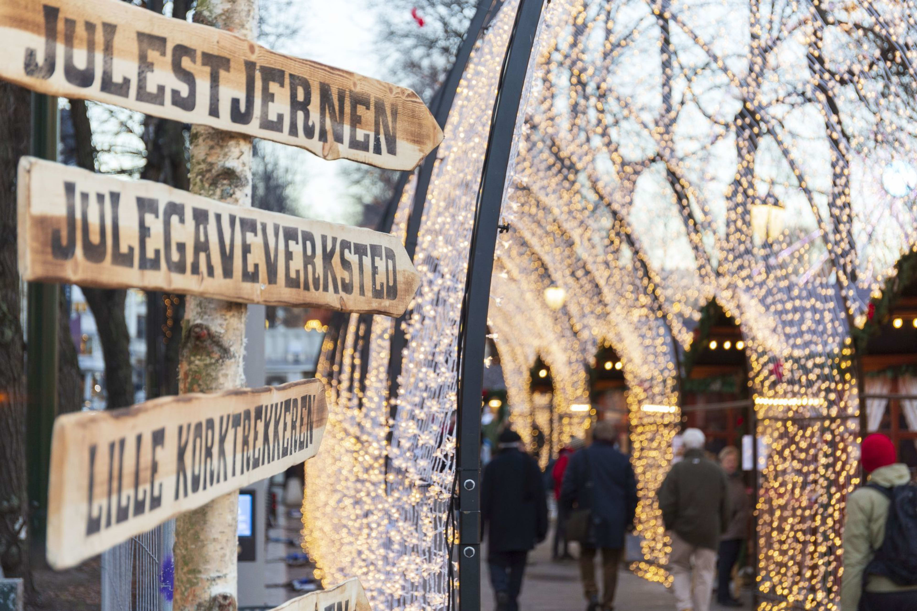 Festliche Holzschilder, die Besucher durch den Weihnachtsmarkt führen, beleuchtet mit funkelnden Lichtern und einer leuchtenden Atmosphäre.