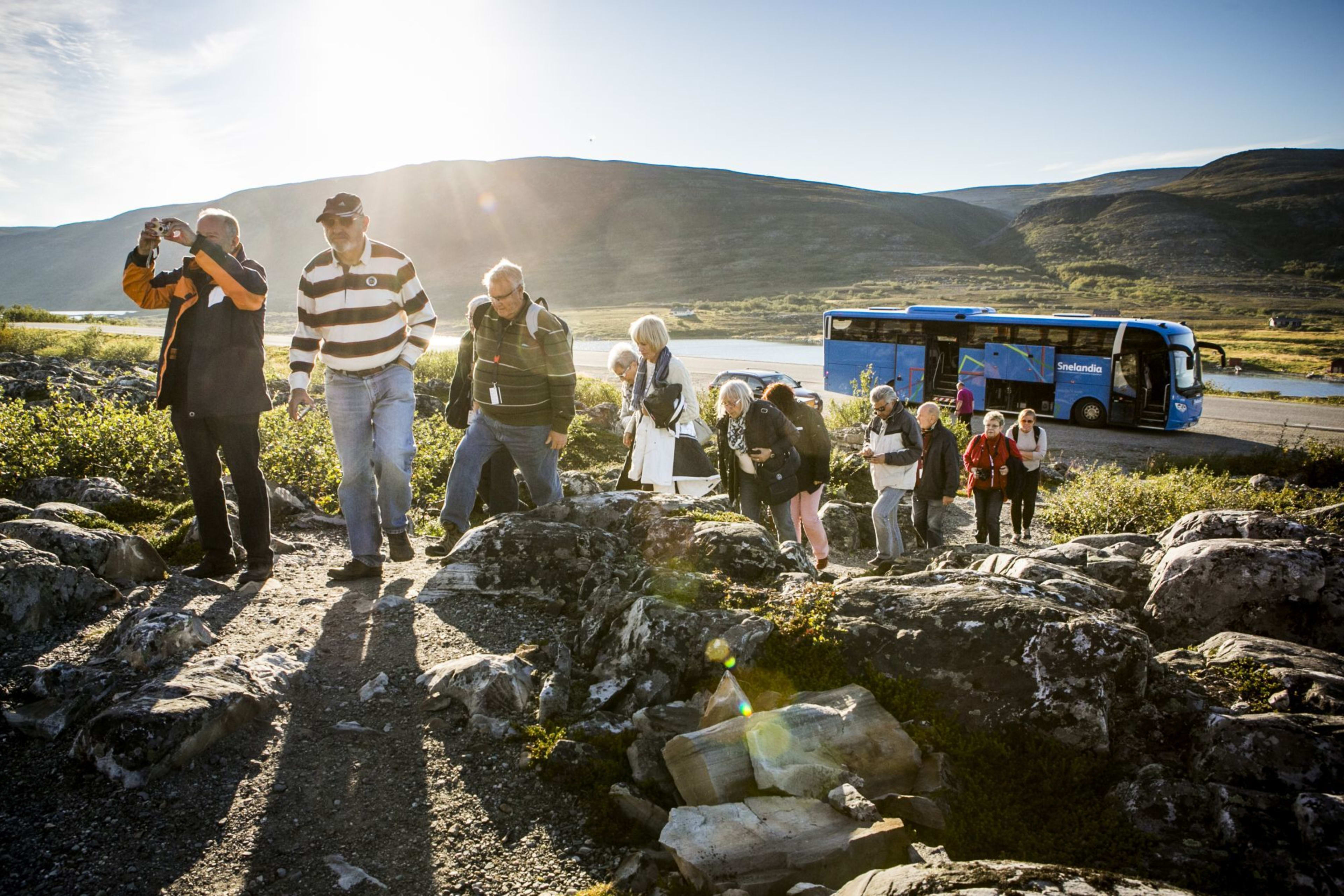 Touristen steigen aus blauem Bus zum Wandern im Gebirge bei goldenem Licht.