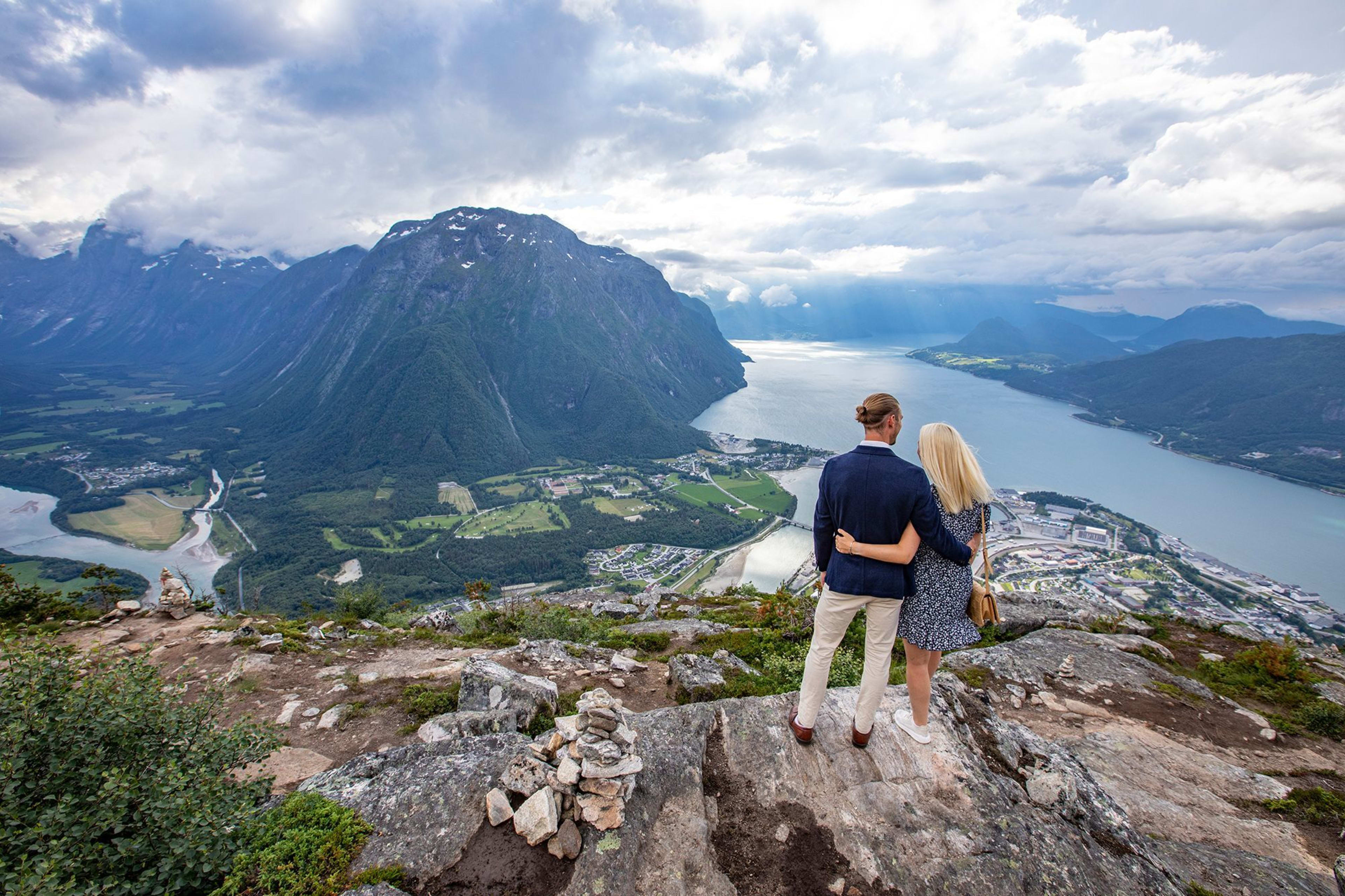 Par på Nesaksla , ser ut over Åndalsnes , elv og fjord under dramatisk himmel.