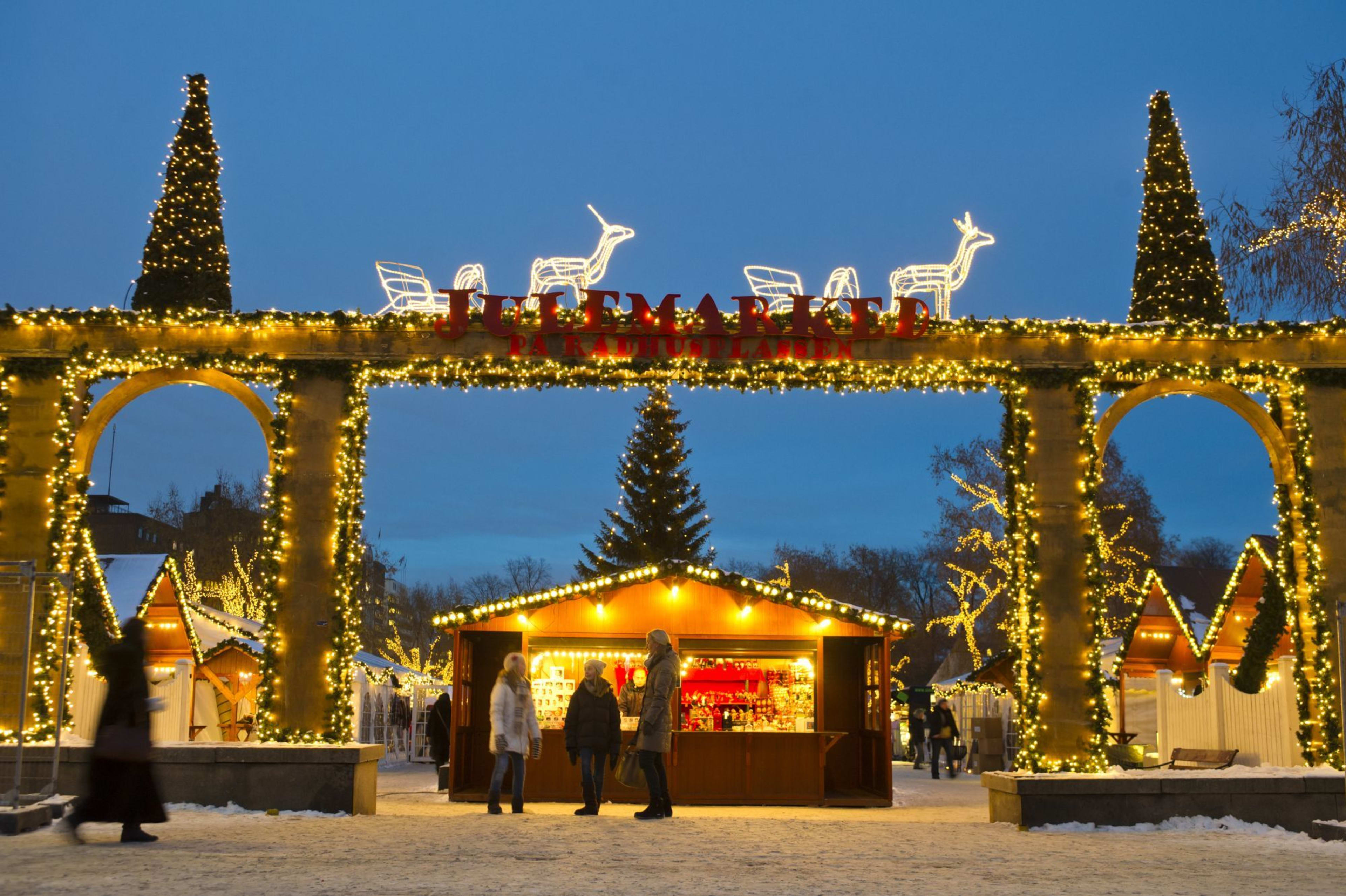Eingang zum Weihnachtsmarkt mit Lichtern und "JULMARKED"-Schild, Rentierdekorationen und festlichen Ständen in einer verschneiten Straße.