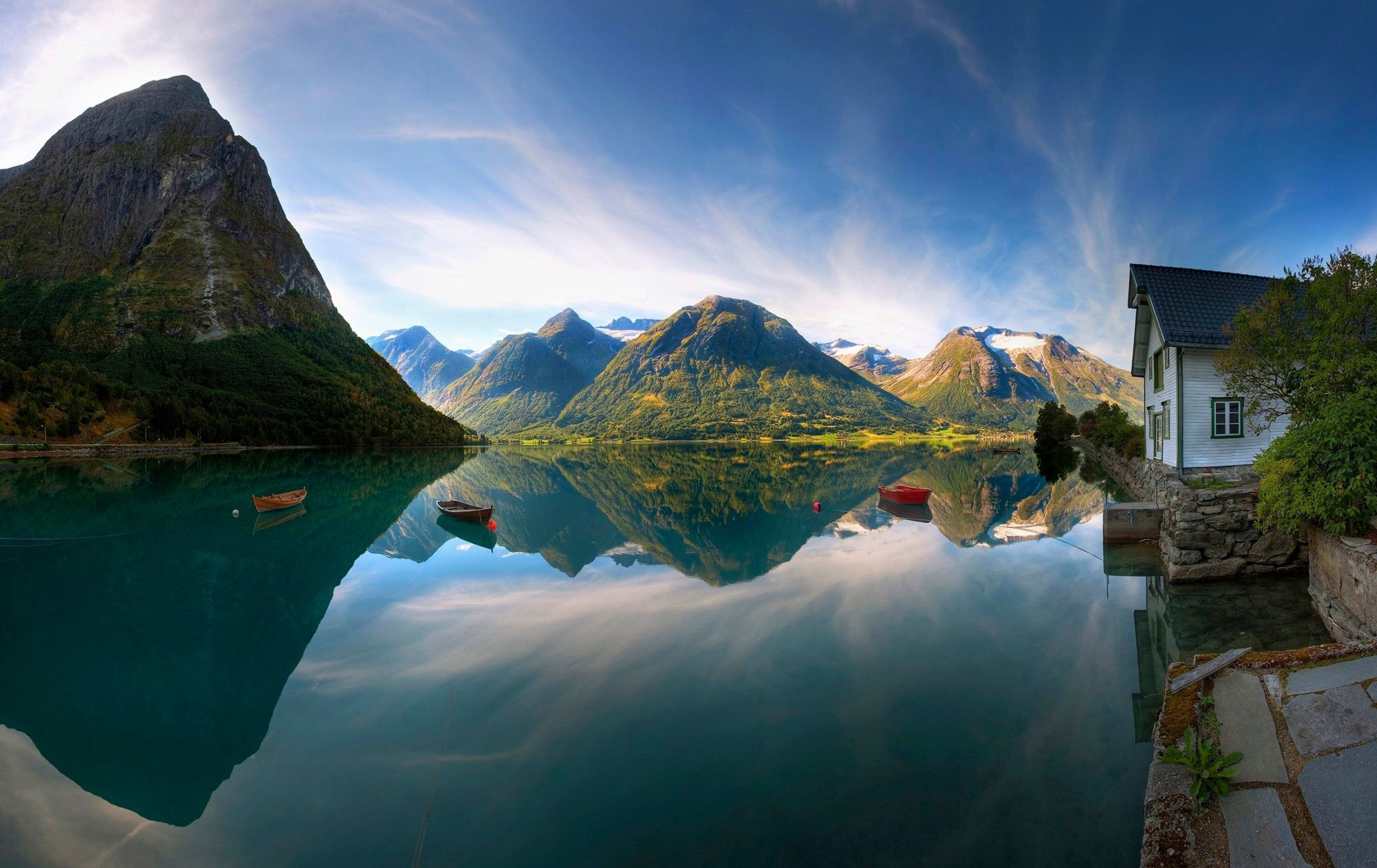 Ruhige Seelandschaft mit kristallklarem Wasser, das schneebedeckte Berge, grüne Hügel und schwimmende Holzboote spiegelt.