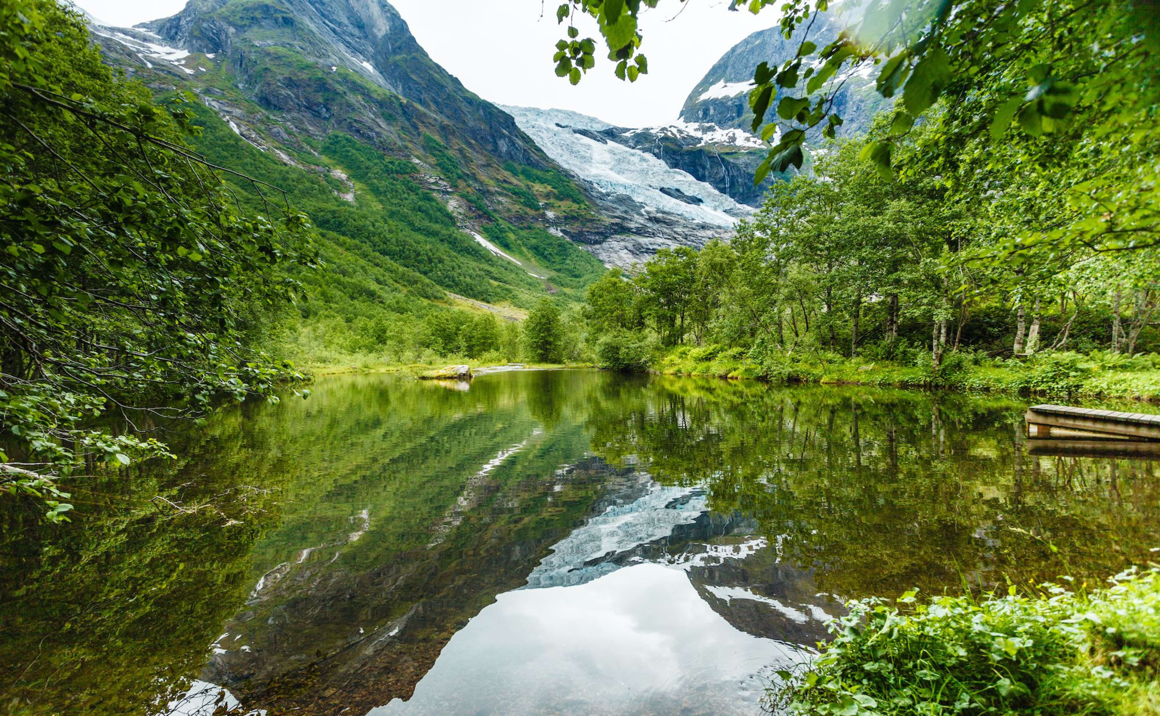 Snow-capped mountains reflect on a still lake by a wooden dock.