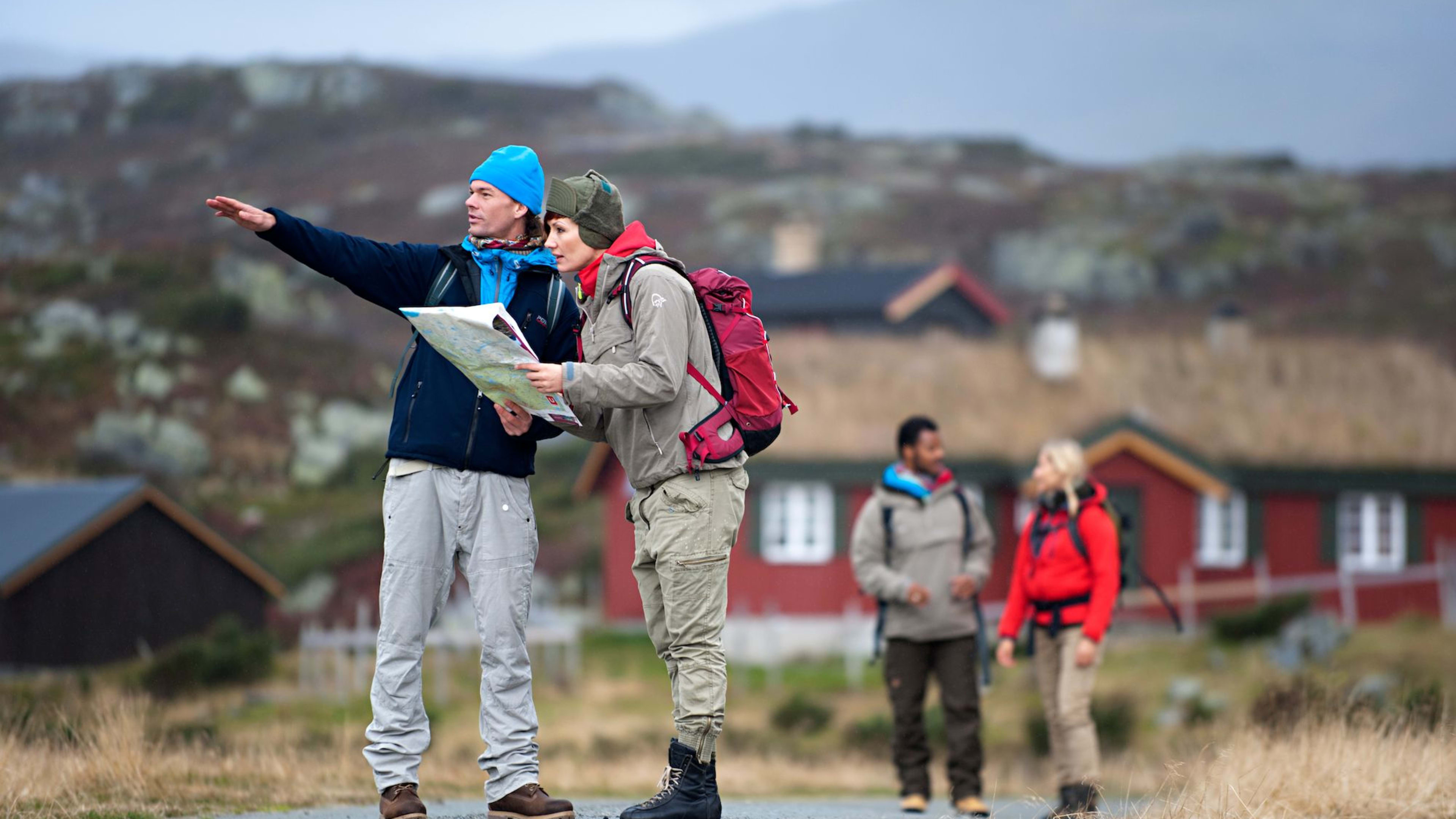 En gruppe turgåere med sekker leser et kart i et røft norsk landskap med hytter i bakgrunnen.