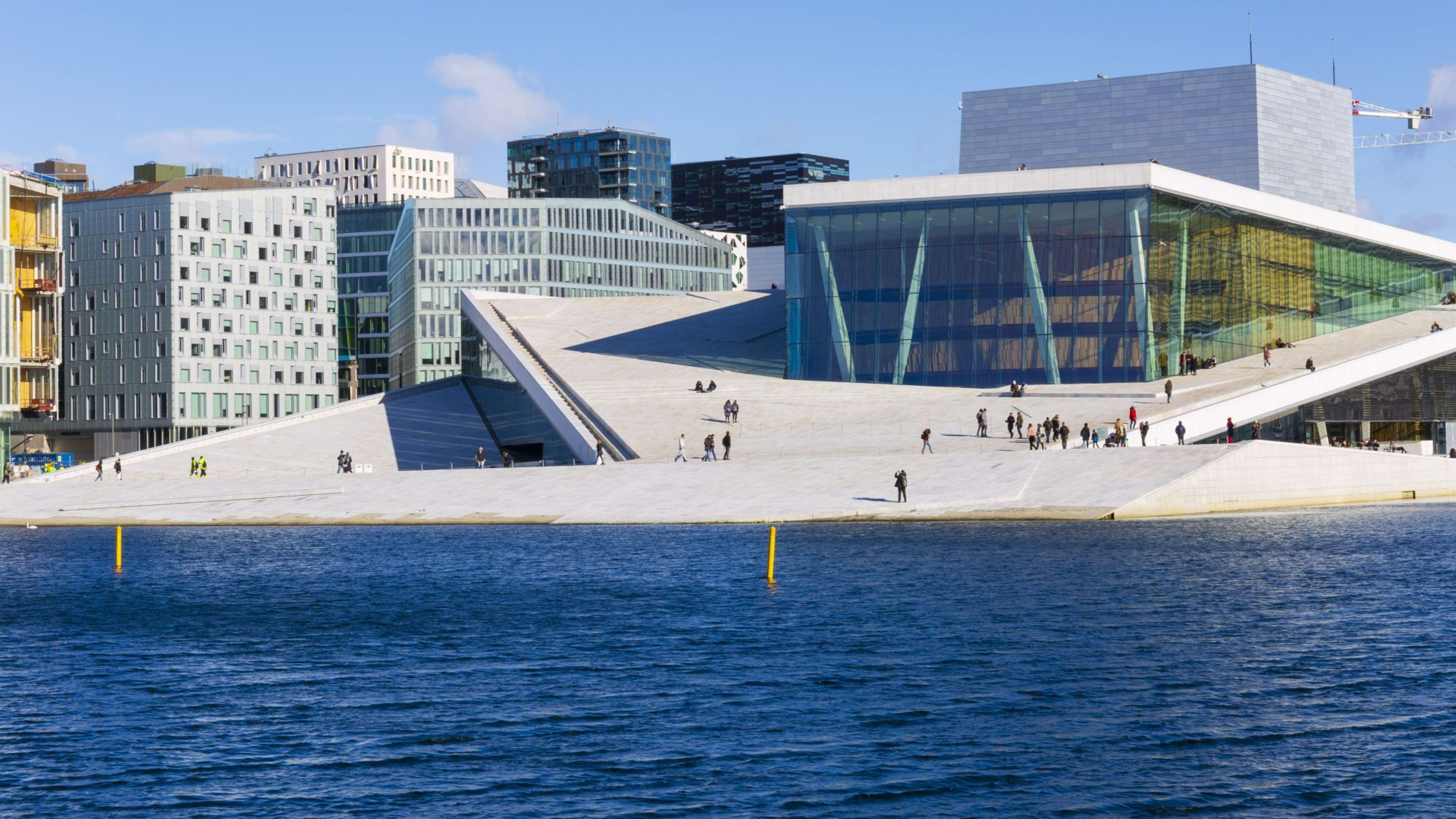Oslo Operahus med moderne skråtak, folk som går på marmorskjeller og refleksjoner i det omkringliggende vannet.