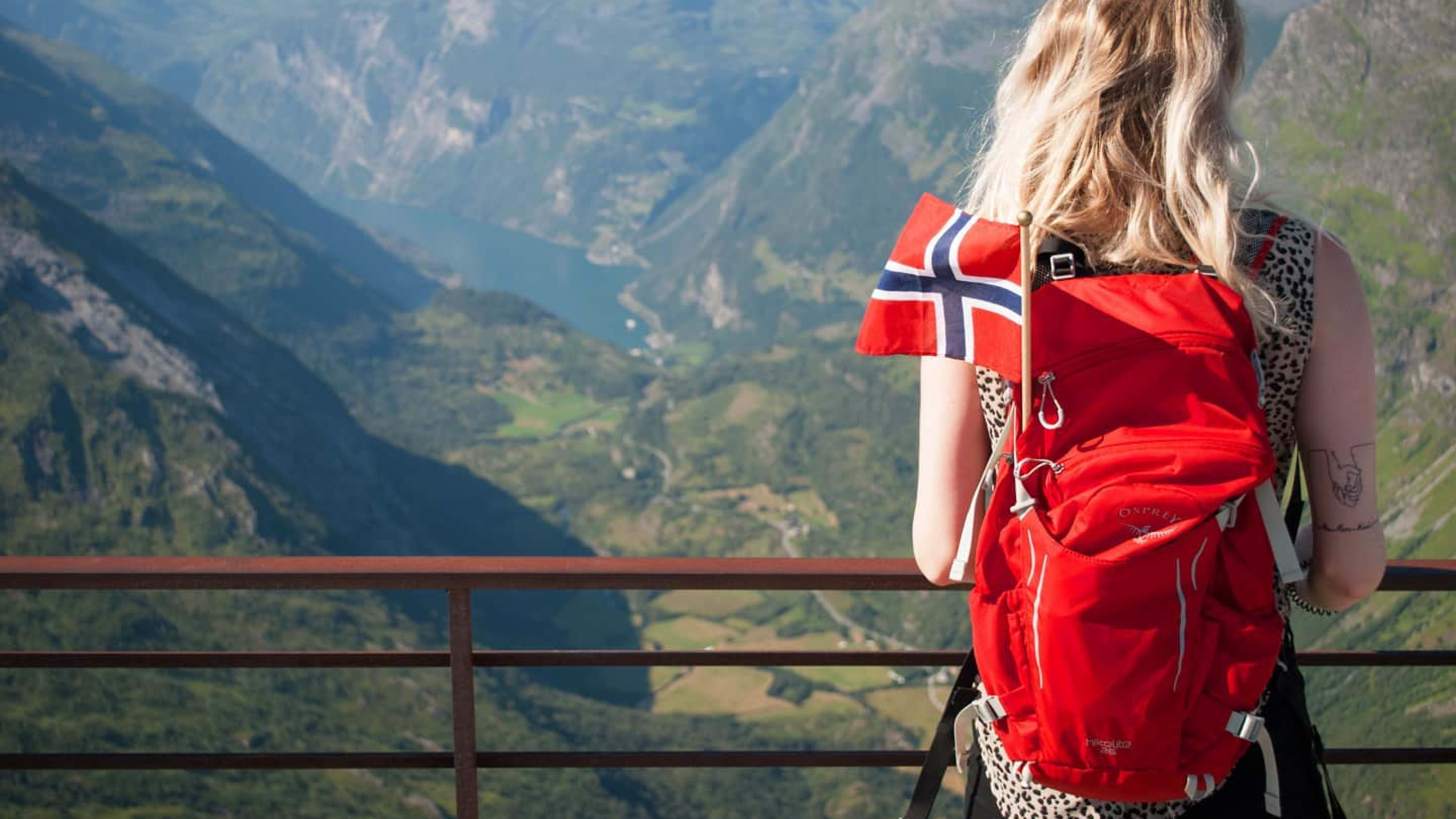 Jente som overser Geiranger og Geirangerfjorden med et norsk flagg i sekken
